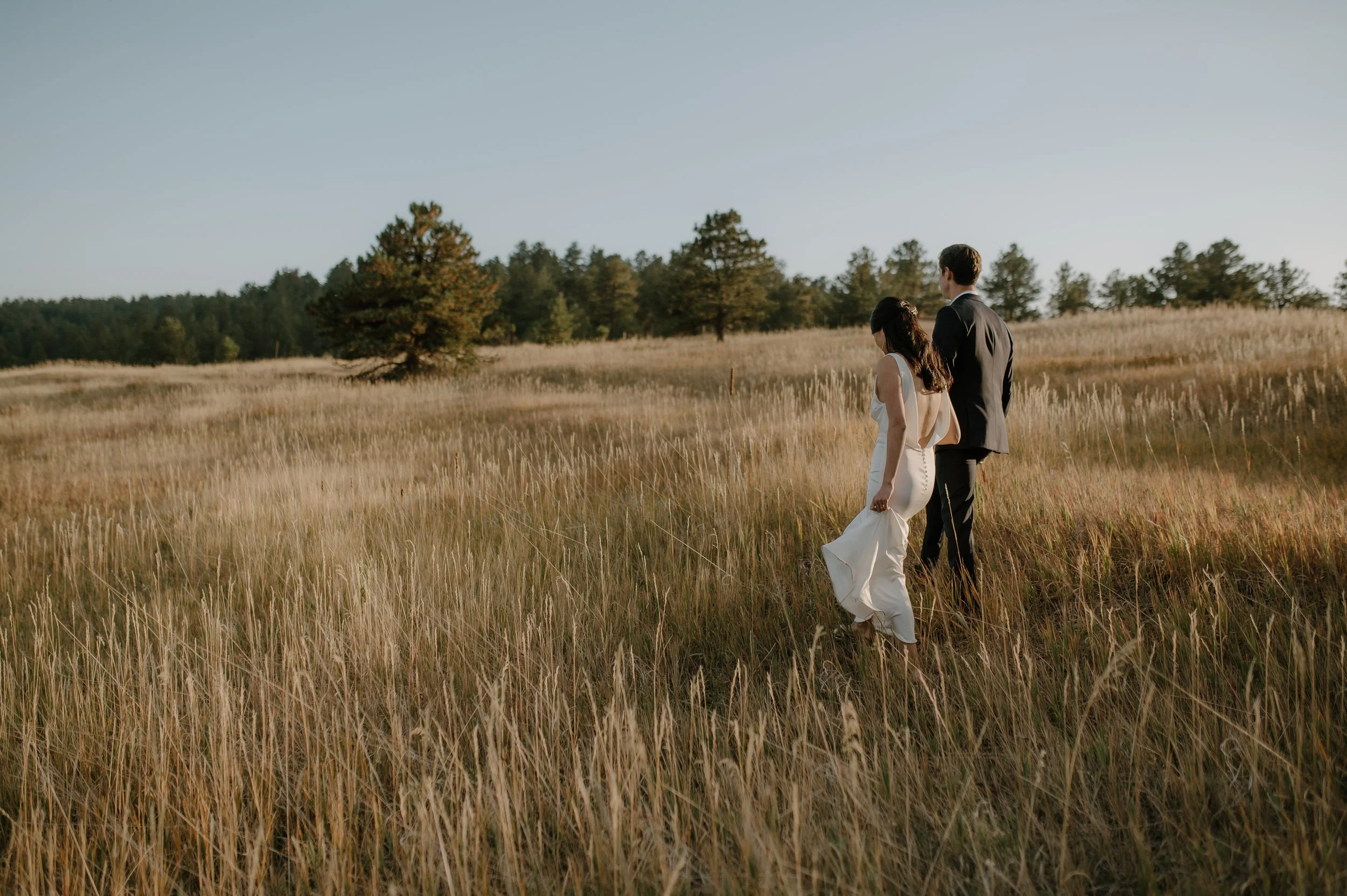 Bride and groom walking hand in hand in a field during sunset