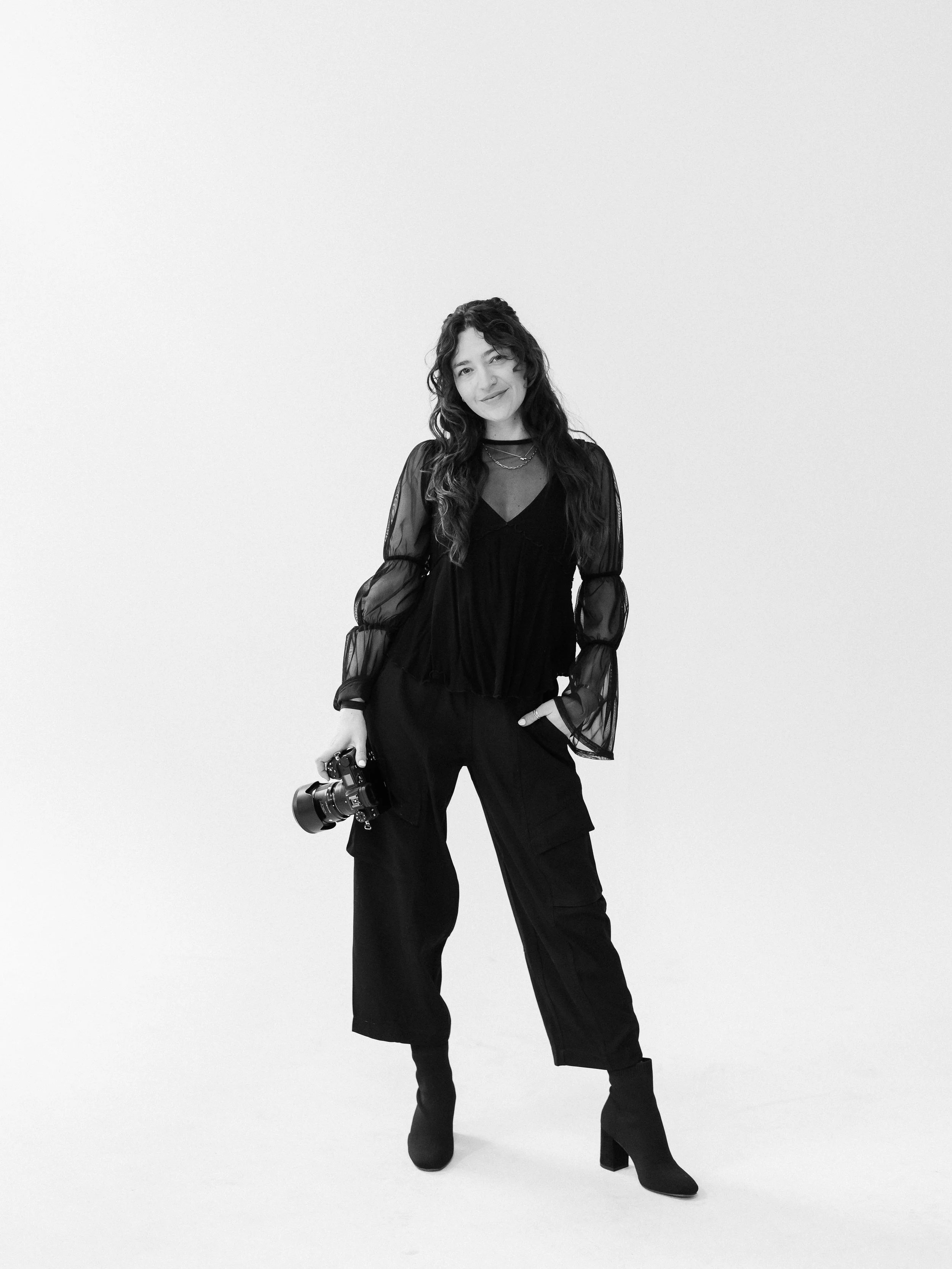 black and white photo of a woman dressed in black holding a camera