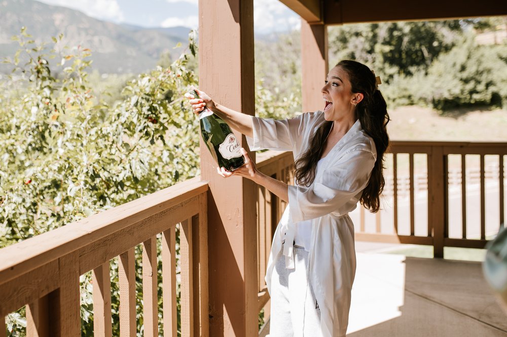  Bride popping champagne while getting ready for her wedding day at cheyenne mountain resort in Colorado Springs   