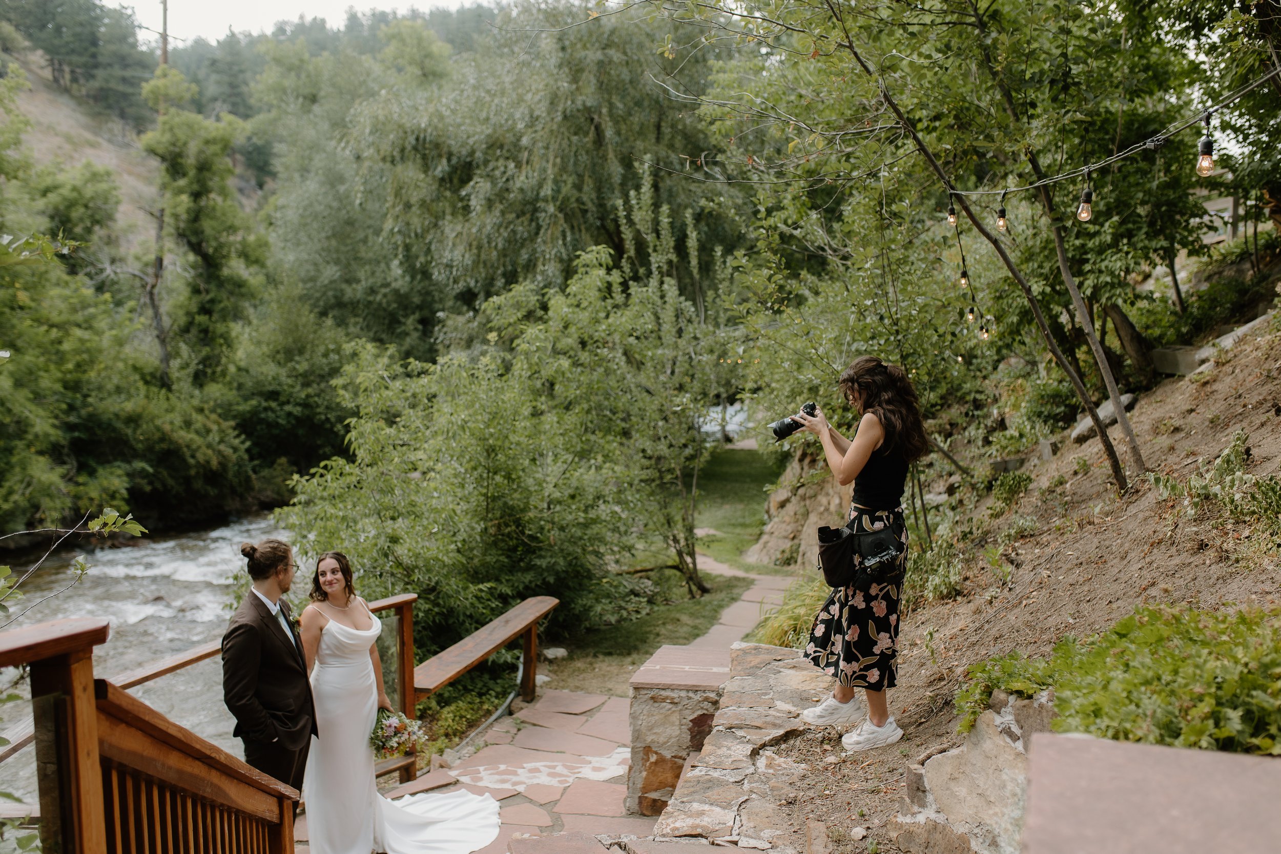 wedding photographer photographing a bride and groom by a river surrounded by leafy trees