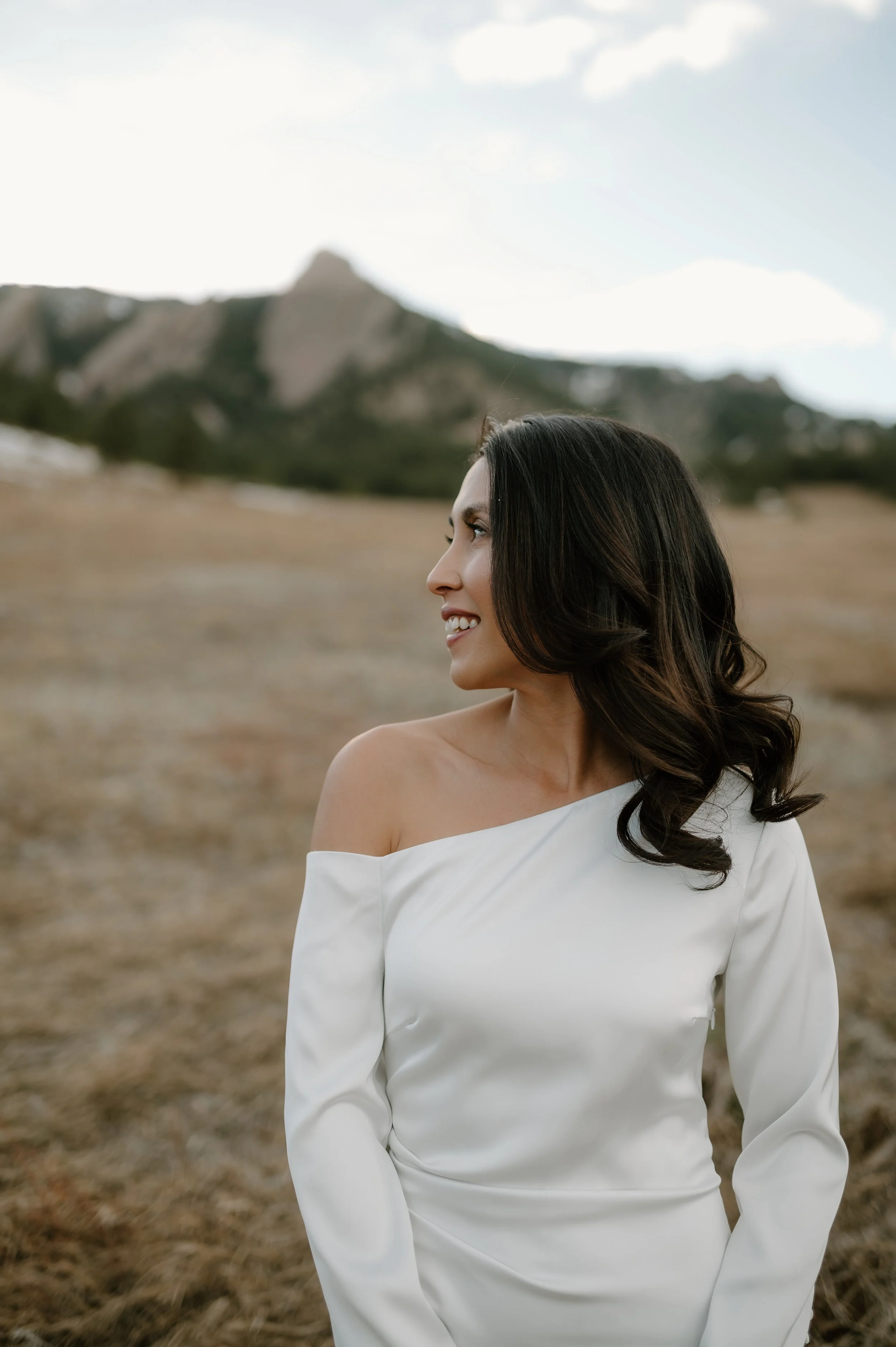 Bride facing camera looking over her shoulder away with flatiron mountains in the distant background.