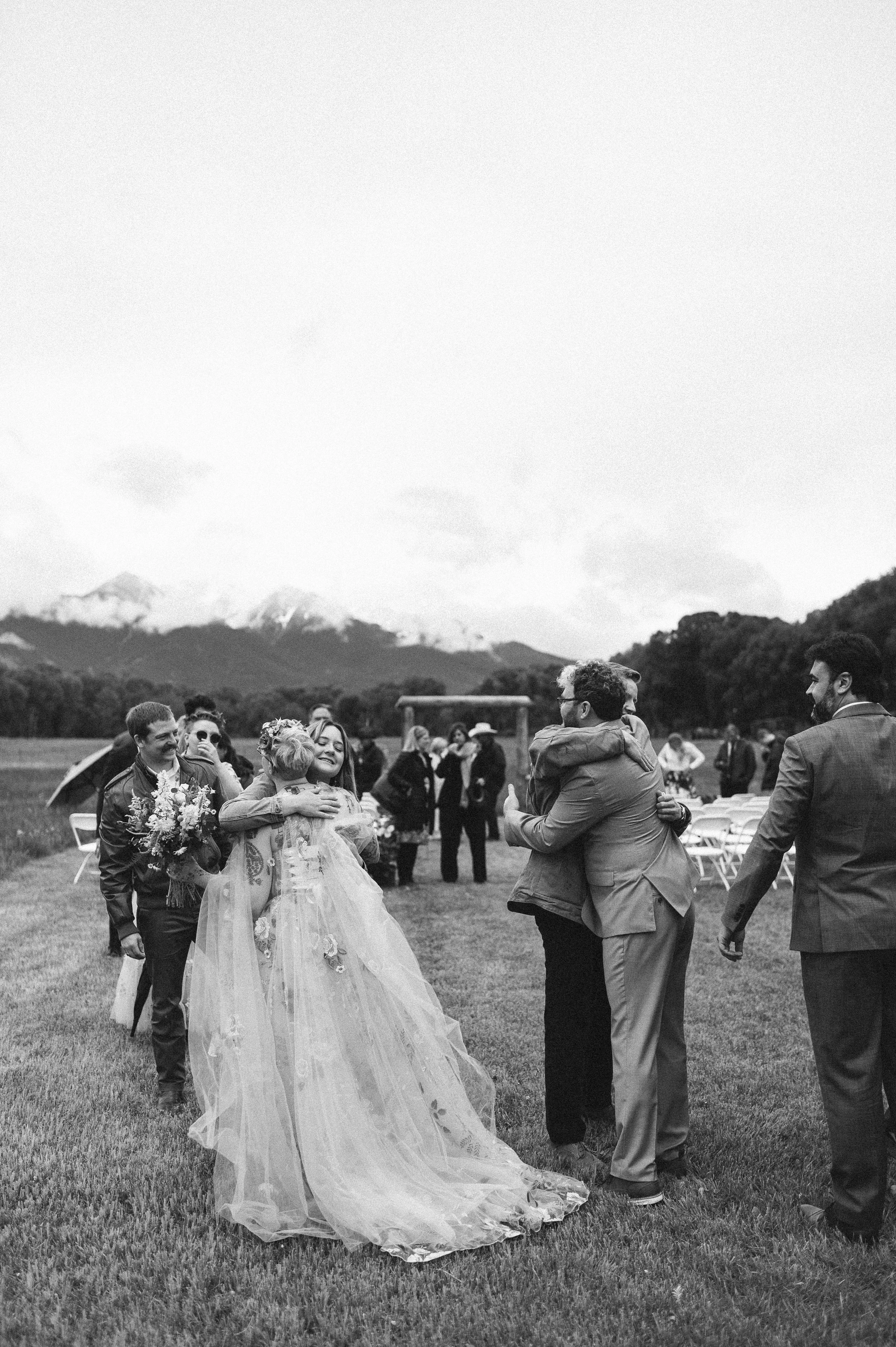 Photo of a bride and groom hugging their guests after their wedding ceremony in front of a mountainous background