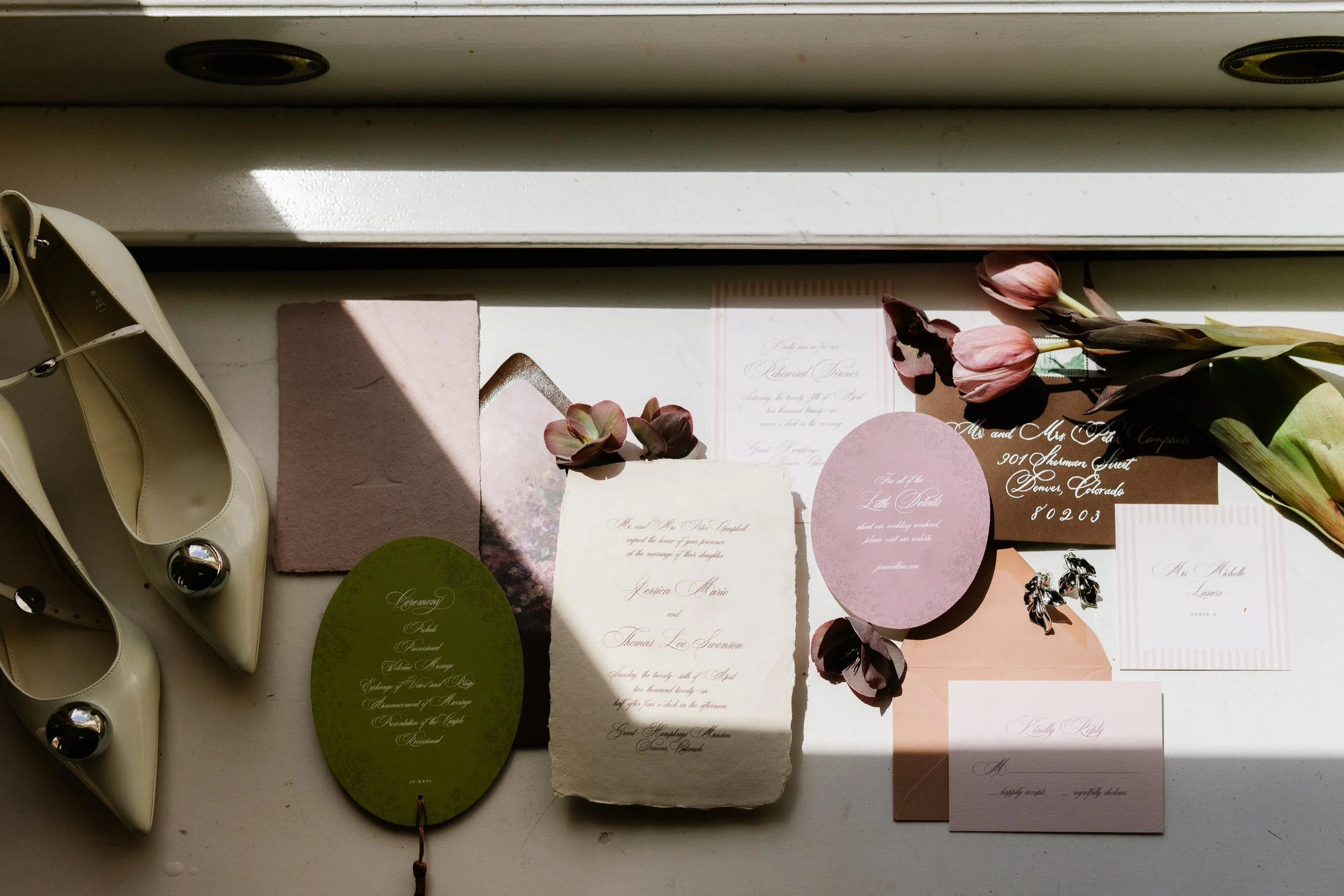 photo of a wedding invitation suite on a windowsill with white, green, and purple paper of different shapes and sizes, white shoes, and pink tulips