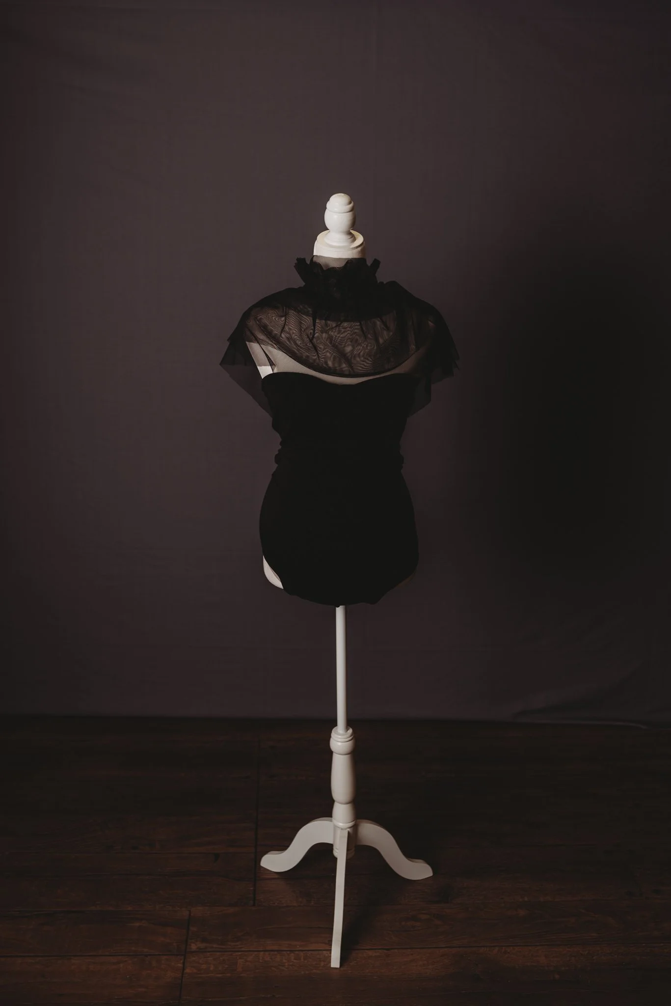 Mannequin with dark sheer shawl on wooden stand against dark background