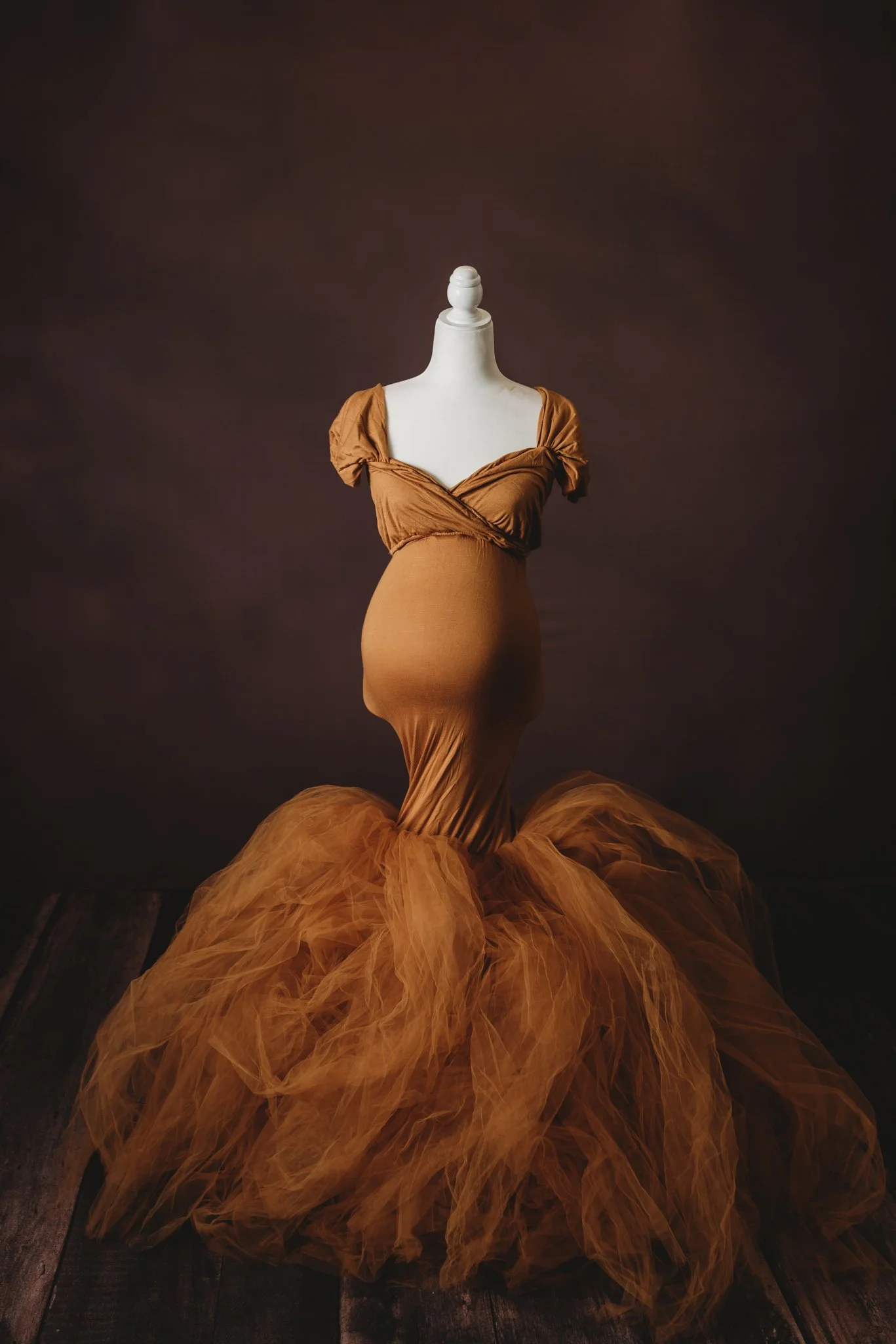 Mannequin wearing an elegant, brown tulle mermaid-style maternity dress against a dark background.
