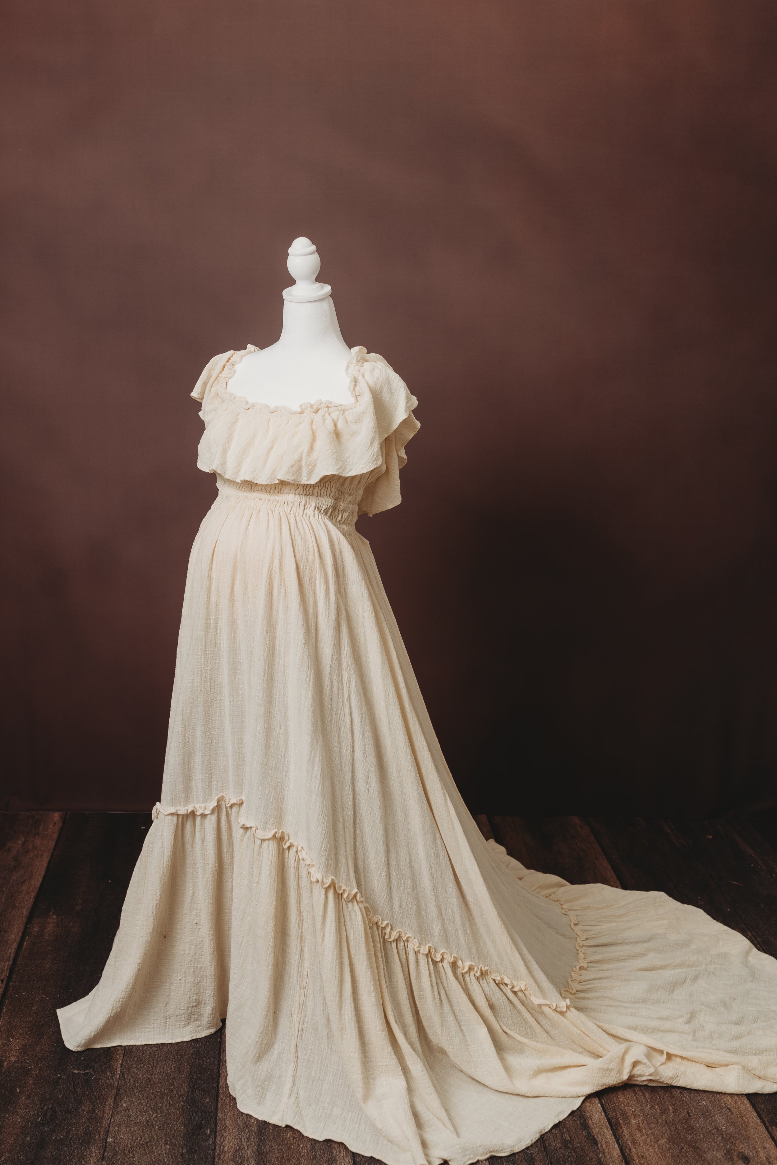A white vintage-style dress with ruffled shoulders and a long flowing skirt is displayed on a mannequin in front of a dark plain background.