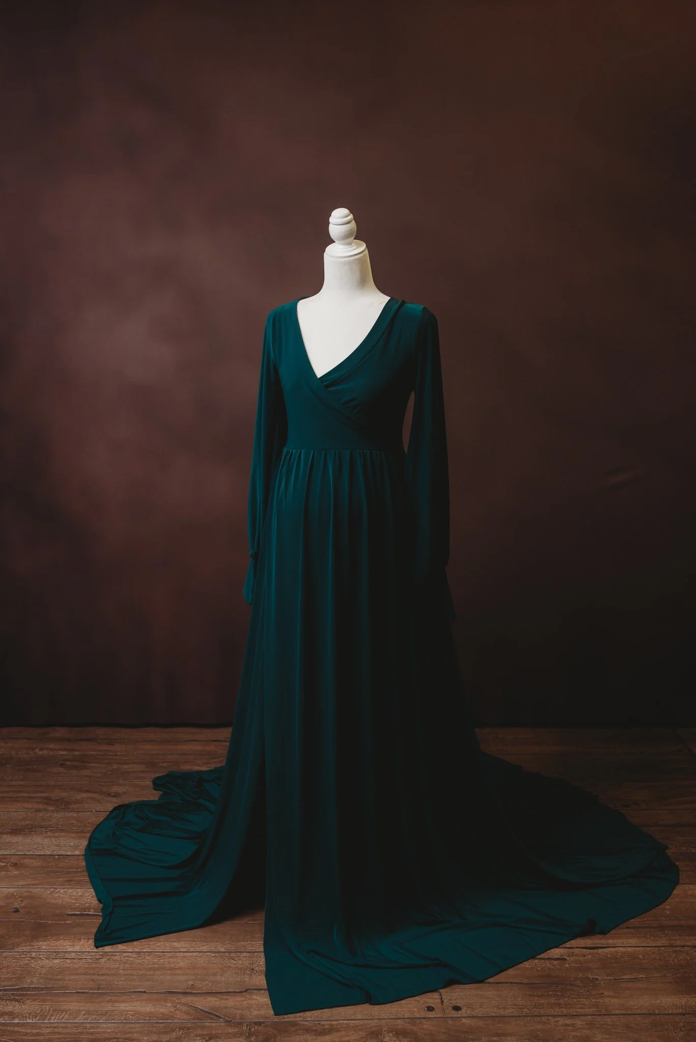 Elegant dark green gown on a mannequin against a brown background.