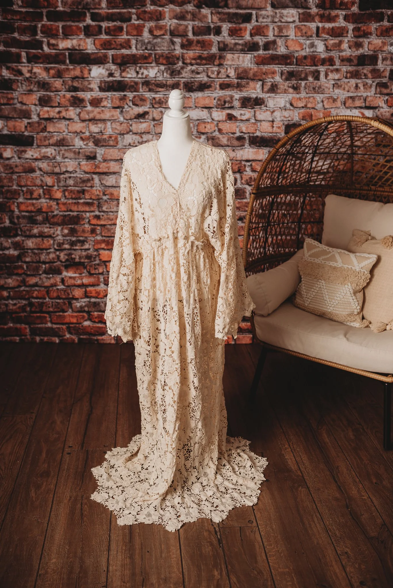 Lace dress on mannequin next to wicker chair with cushions, brick wall background