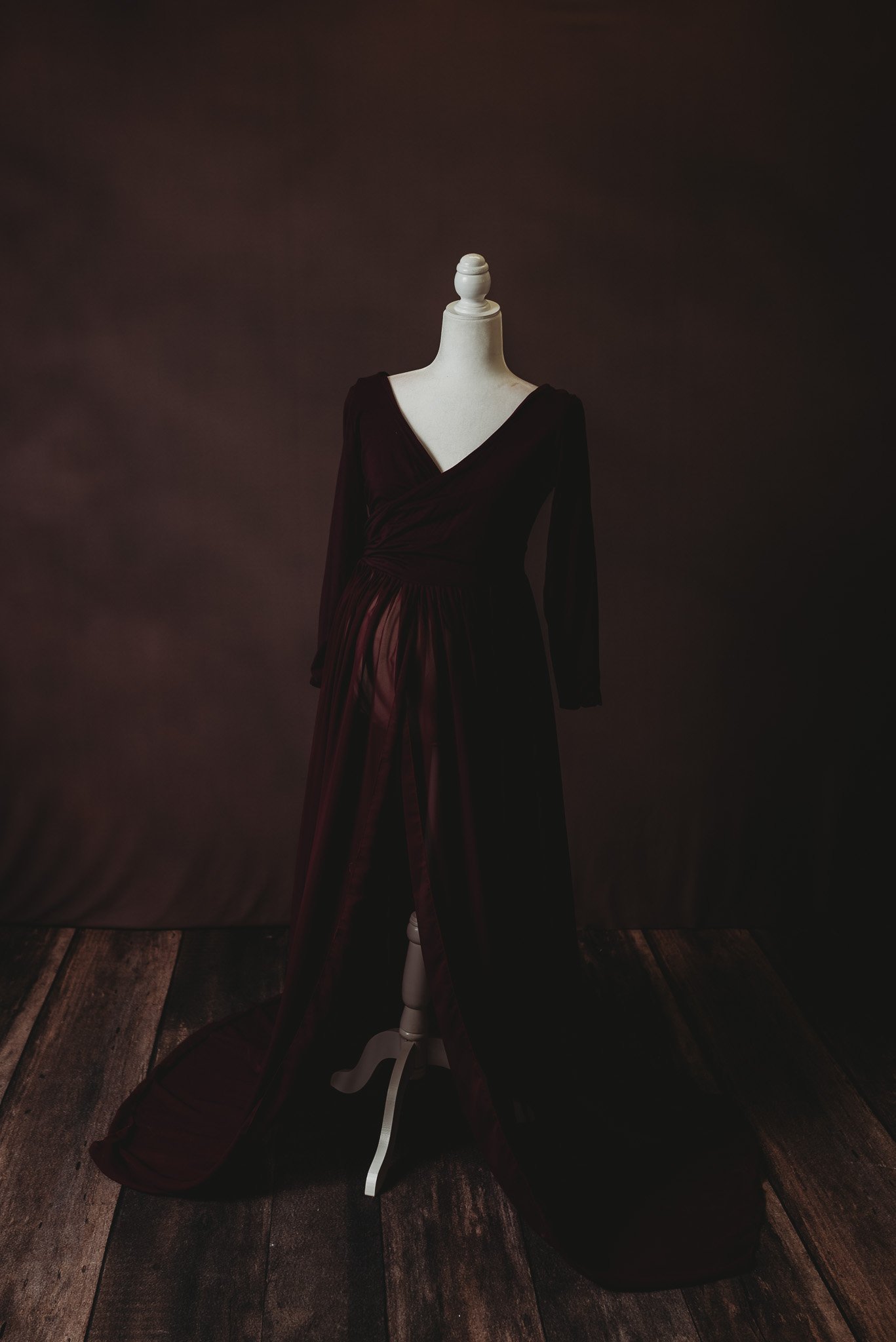 Mannequin displaying a long dark dress with a deep V-neckline, set against a dark background on wooden flooring.