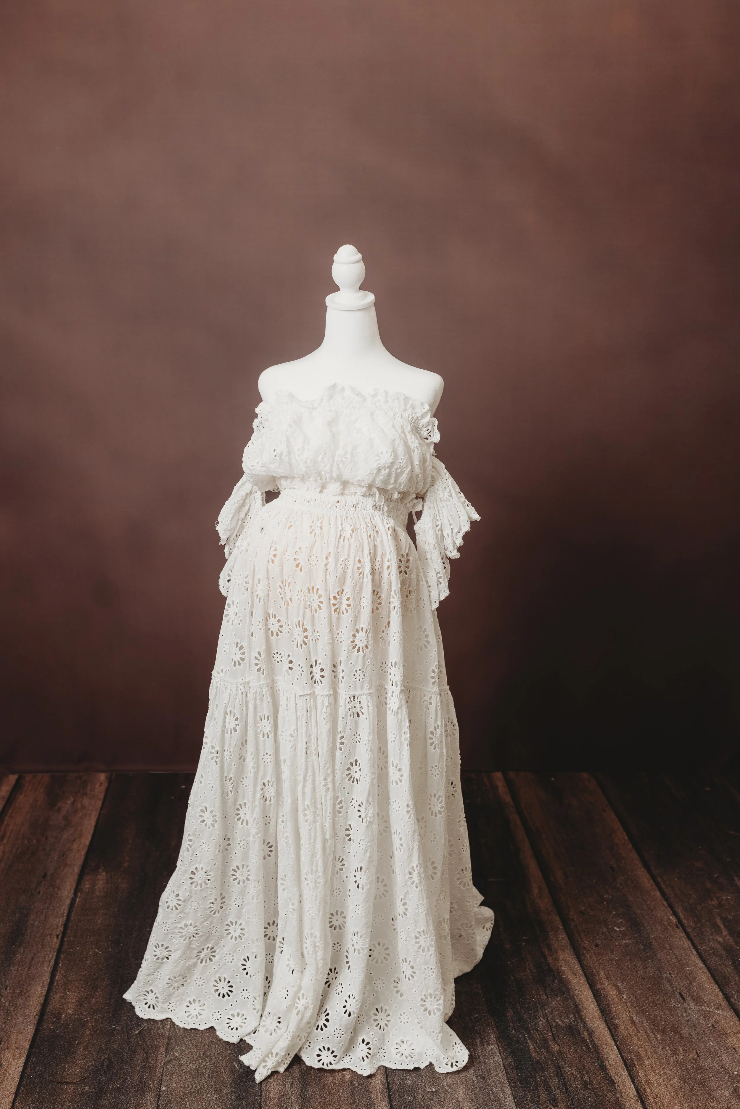 White dress with eyelet embroidery displayed on a mannequin against a brown background.