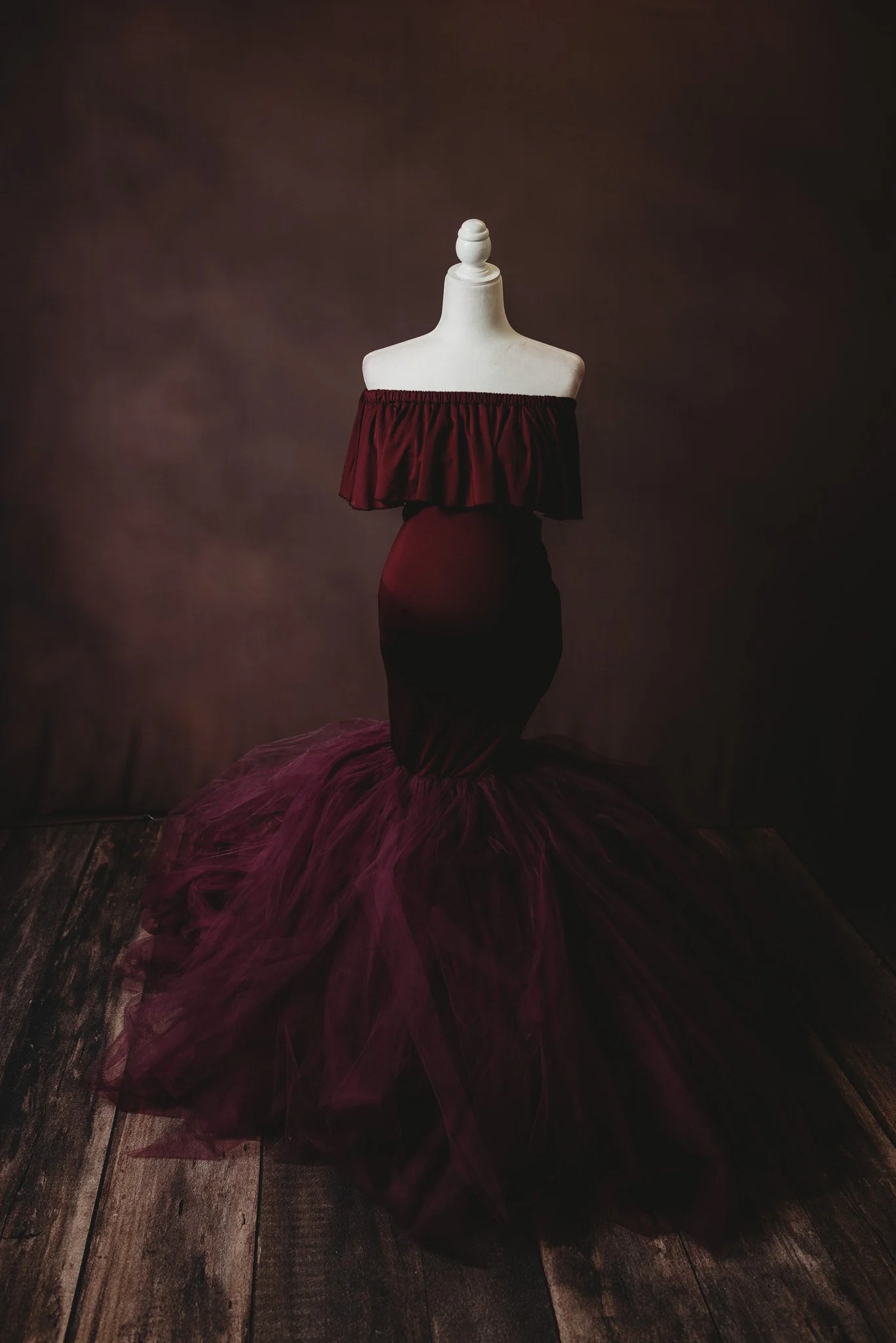 Mannequin wearing an off-shoulder burgundy mermaid gown with tulle skirt.