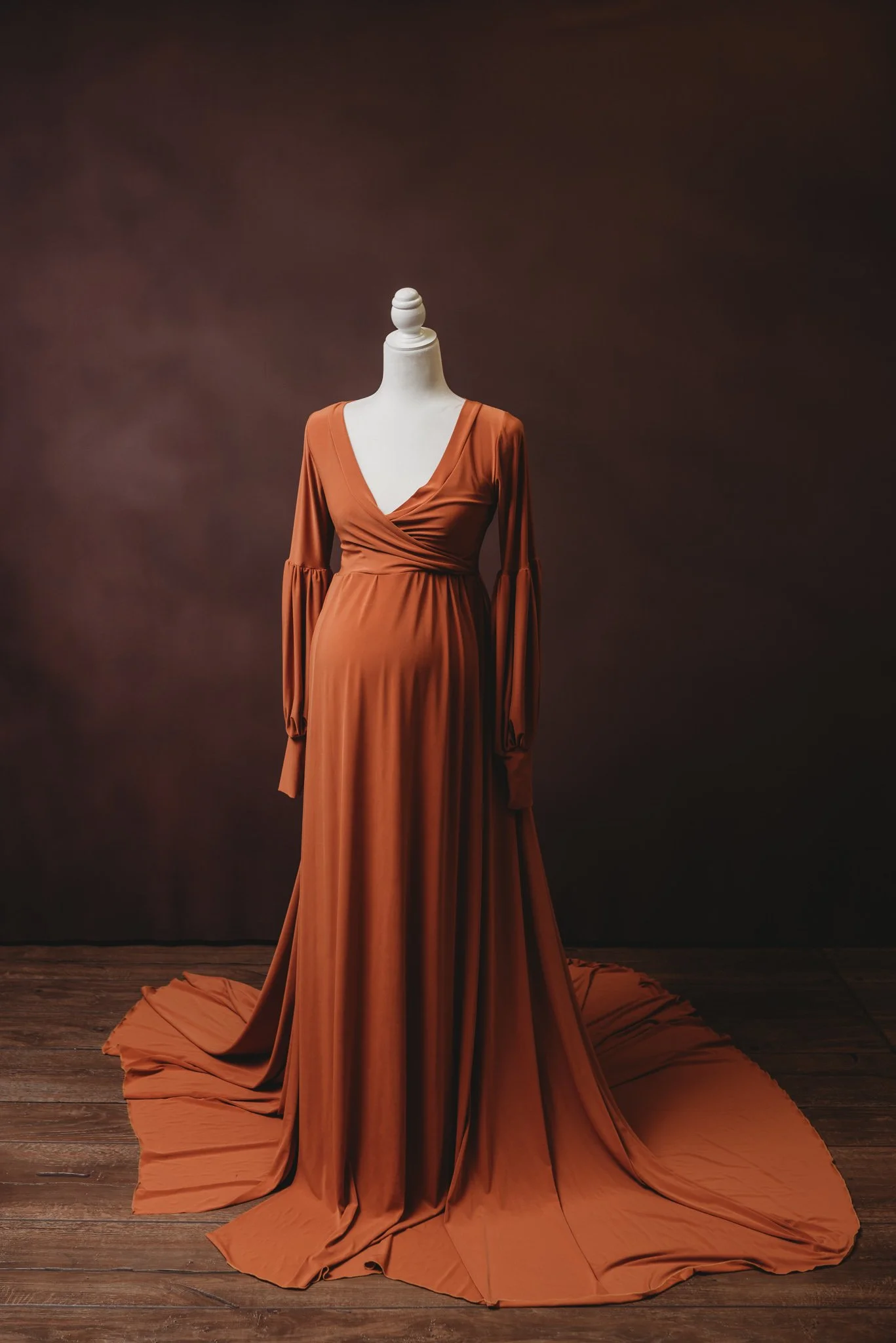 Mannequin wearing a long orange gown with a deep V-neckline and flowing skirt, set against a dark background.