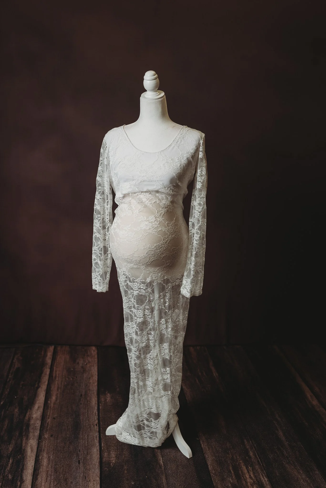 White lace maternity dress on a dress form, wooden floor background.