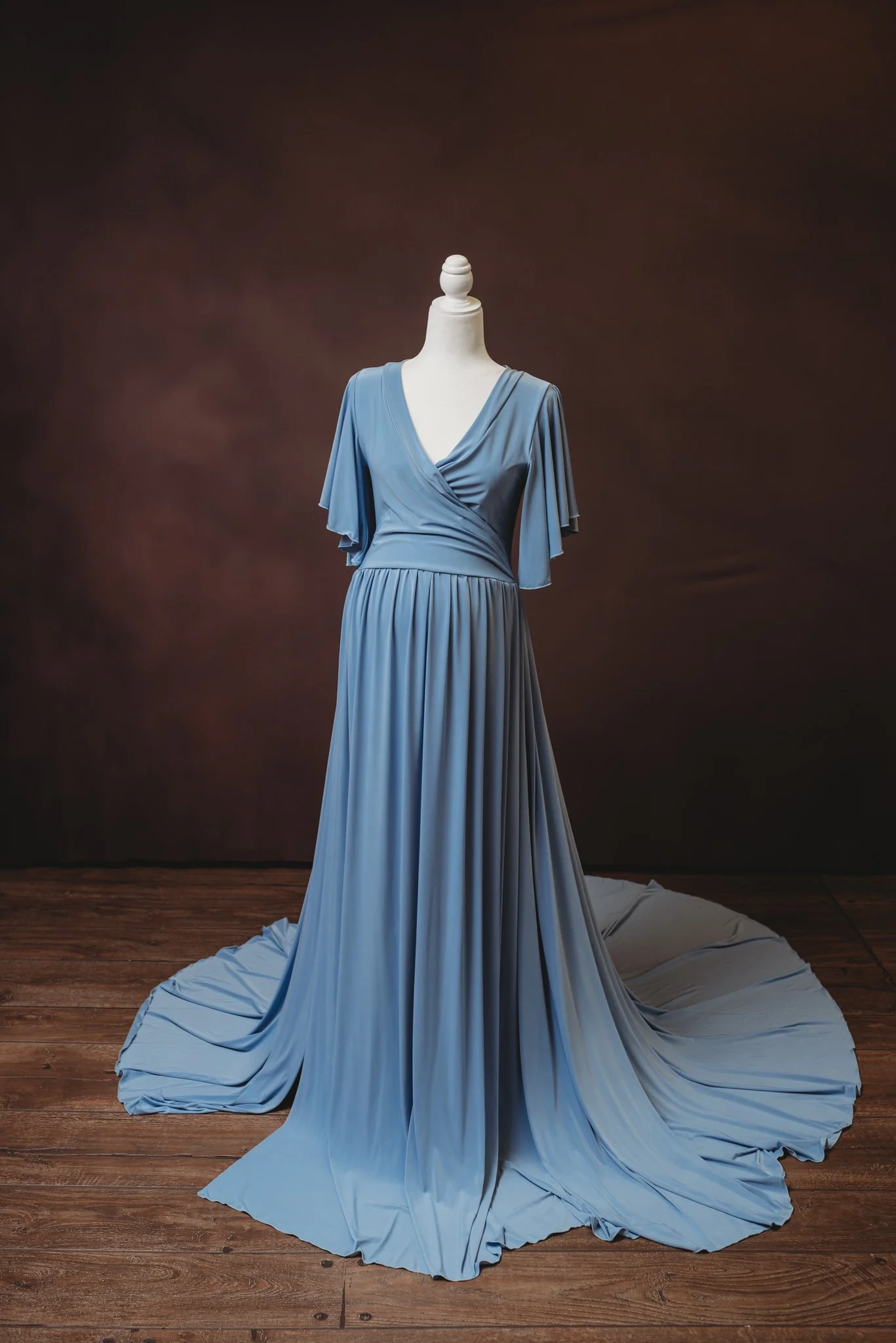 Elegant blue evening gown on mannequin with flutter sleeves and flowing train.