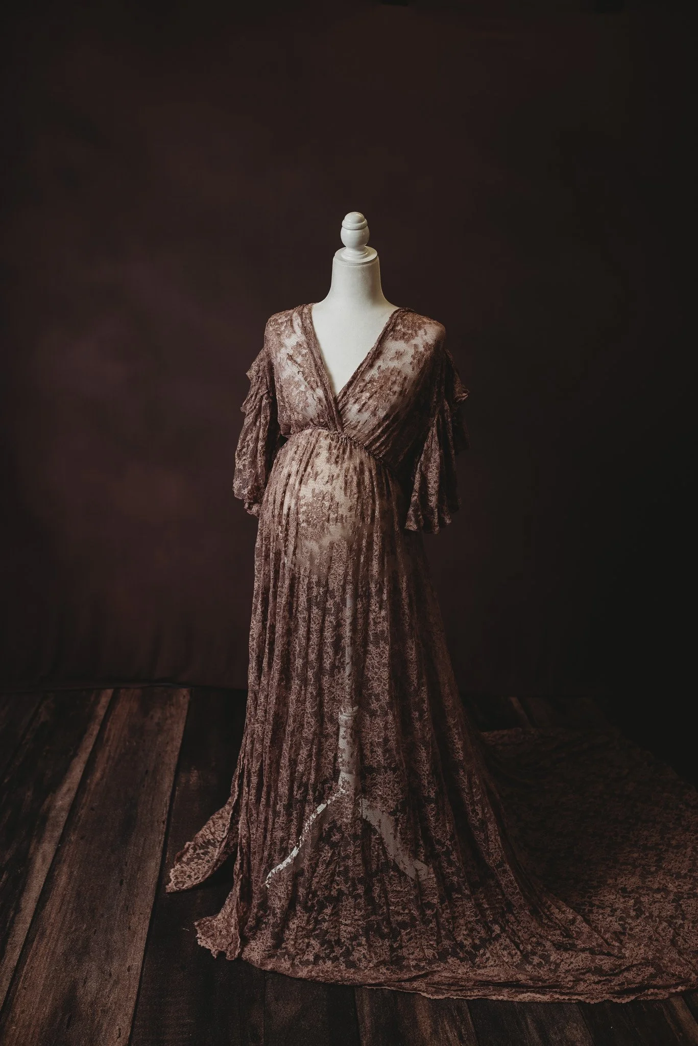 Elegant lace maternity dress on mannequin with dark background.