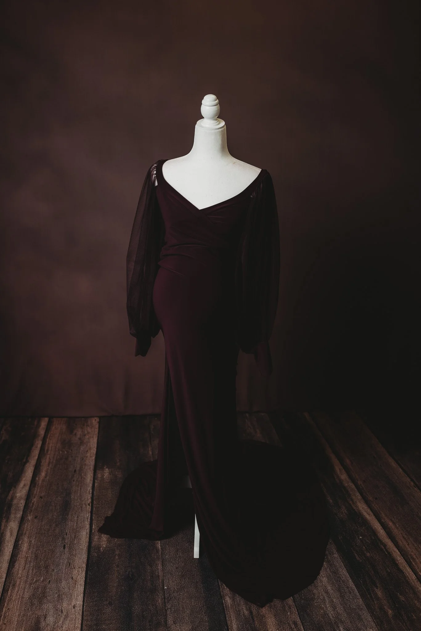 Dark brown long-sleeve dress on a mannequin with a wooden floor and brown background.