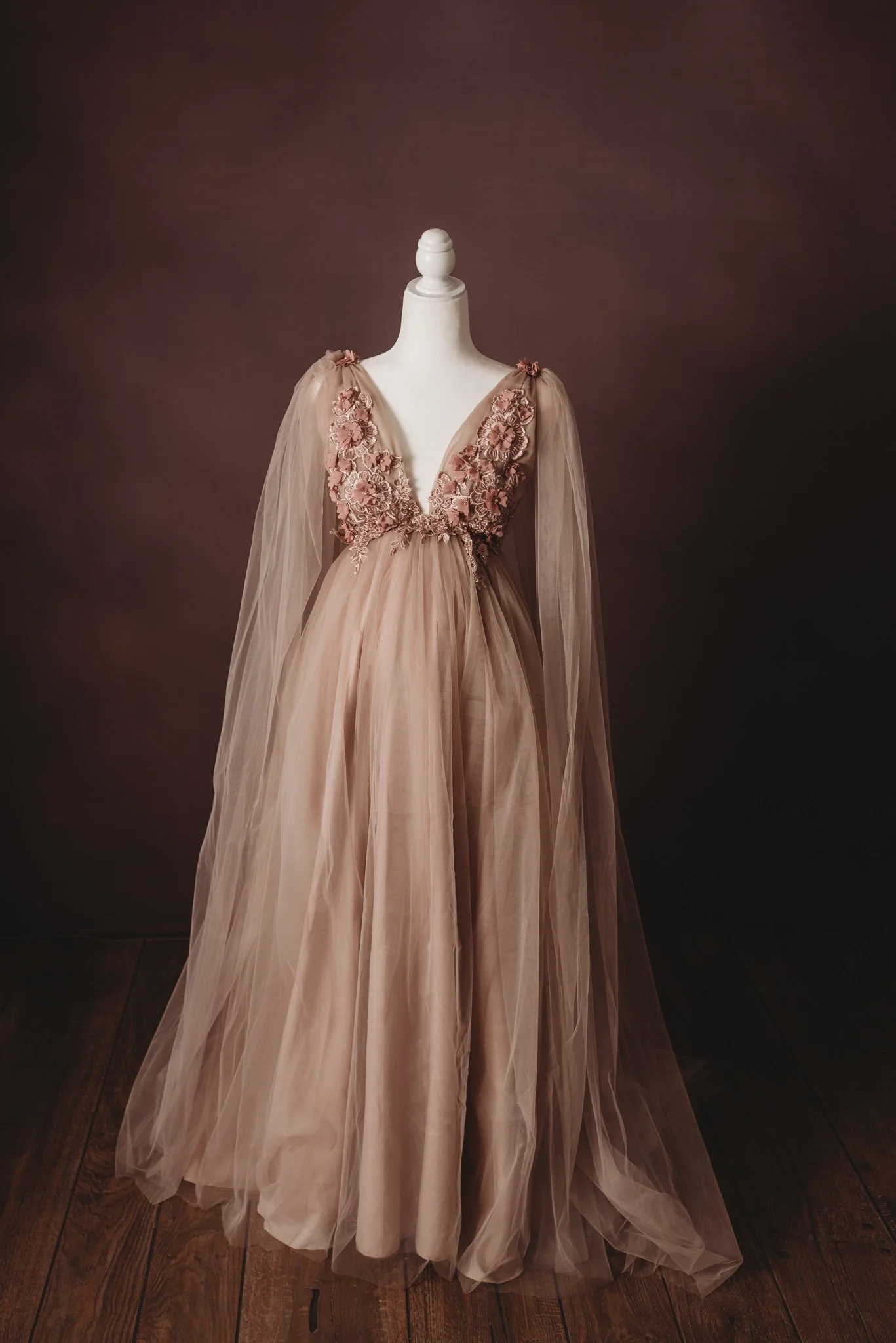 Elegant pink maternity dress with floral embellishments on a mannequin against a dark background.