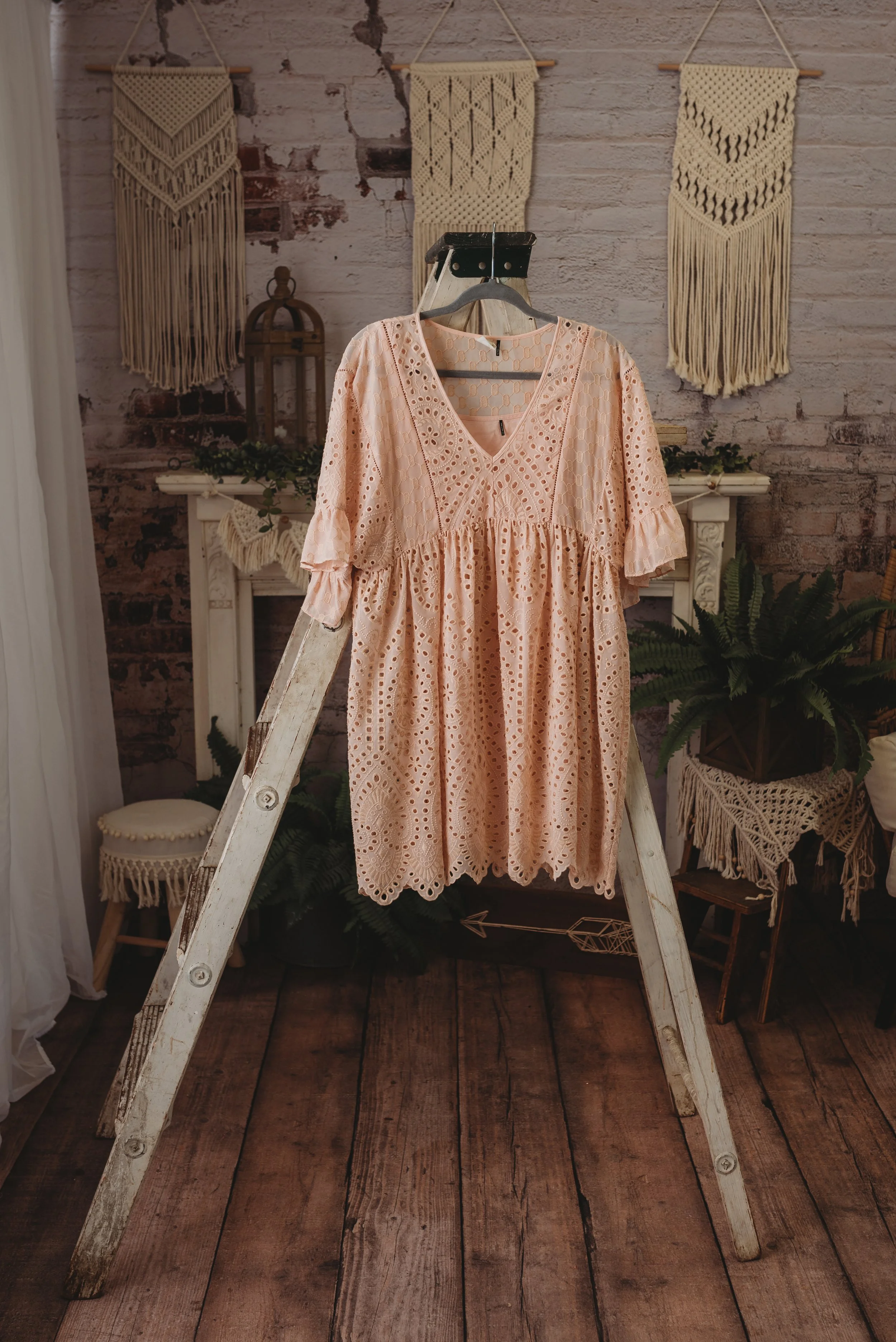 Peach lace dress on wooden ladder, rustic background, macramé wall hangings.