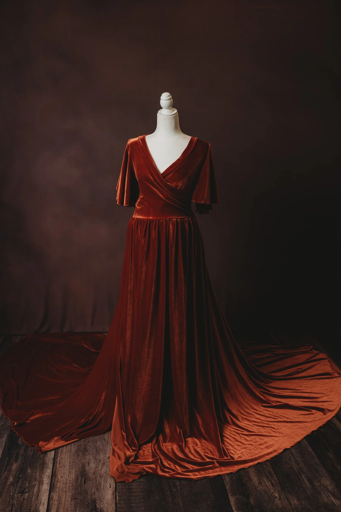 Elegant maroon velvet gown on mannequin with flowing train, set against dark background.