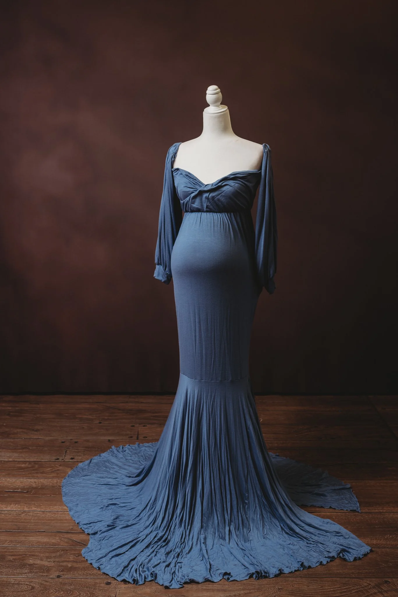 Mannequin wearing a long blue maternity gown with flowing train, brown background