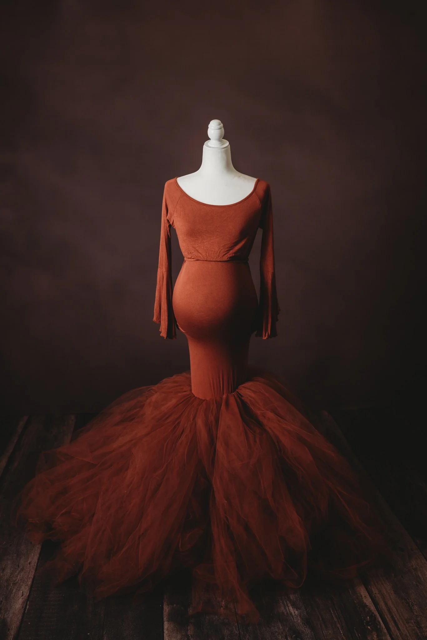 Rust-colored maternity gown on a mannequin against a dark background.