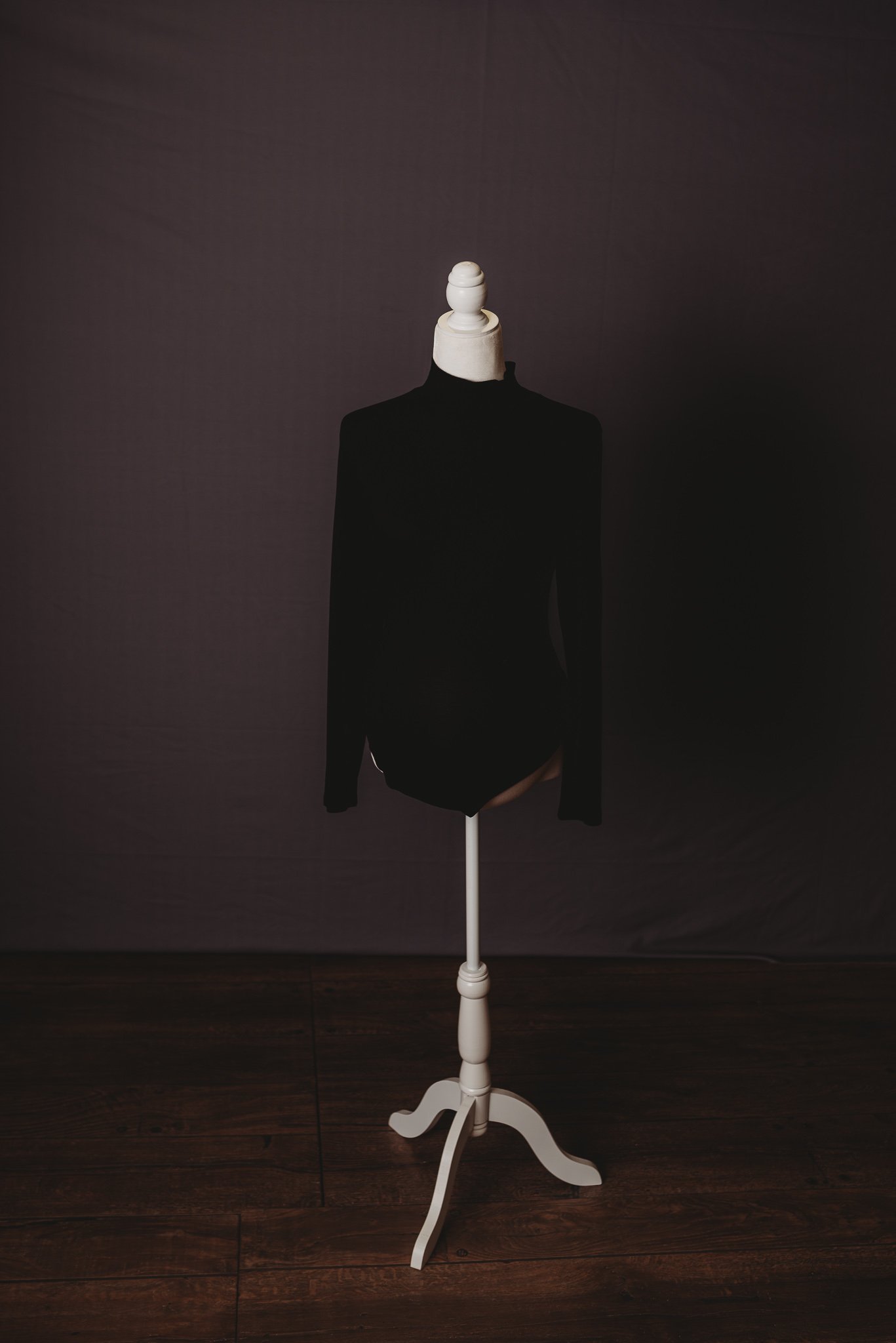 Black long-sleeve bodysuit on white mannequin against dark background
