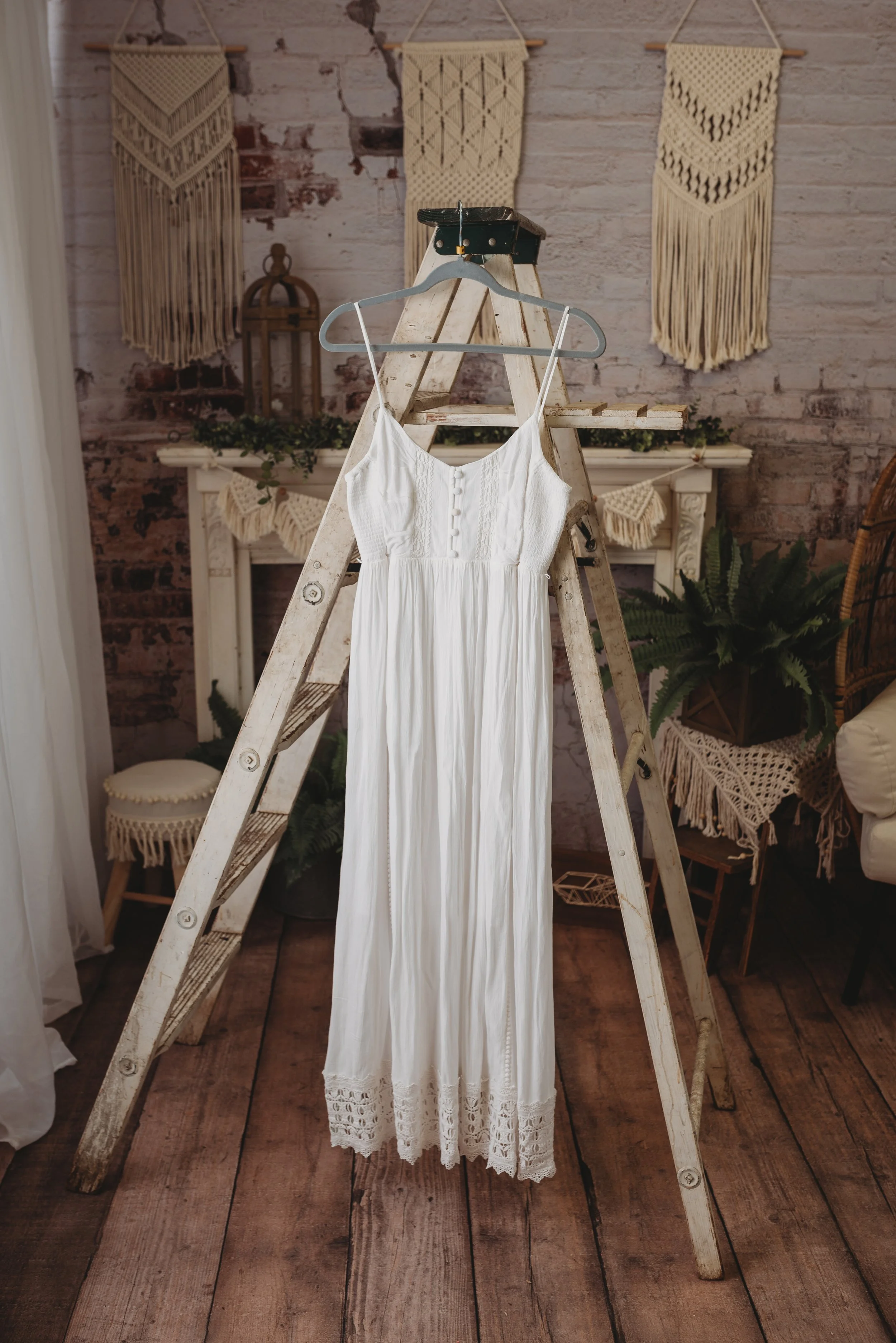 White bohemian dress hanging on a wooden ladder with macramé wall hangings in the background.