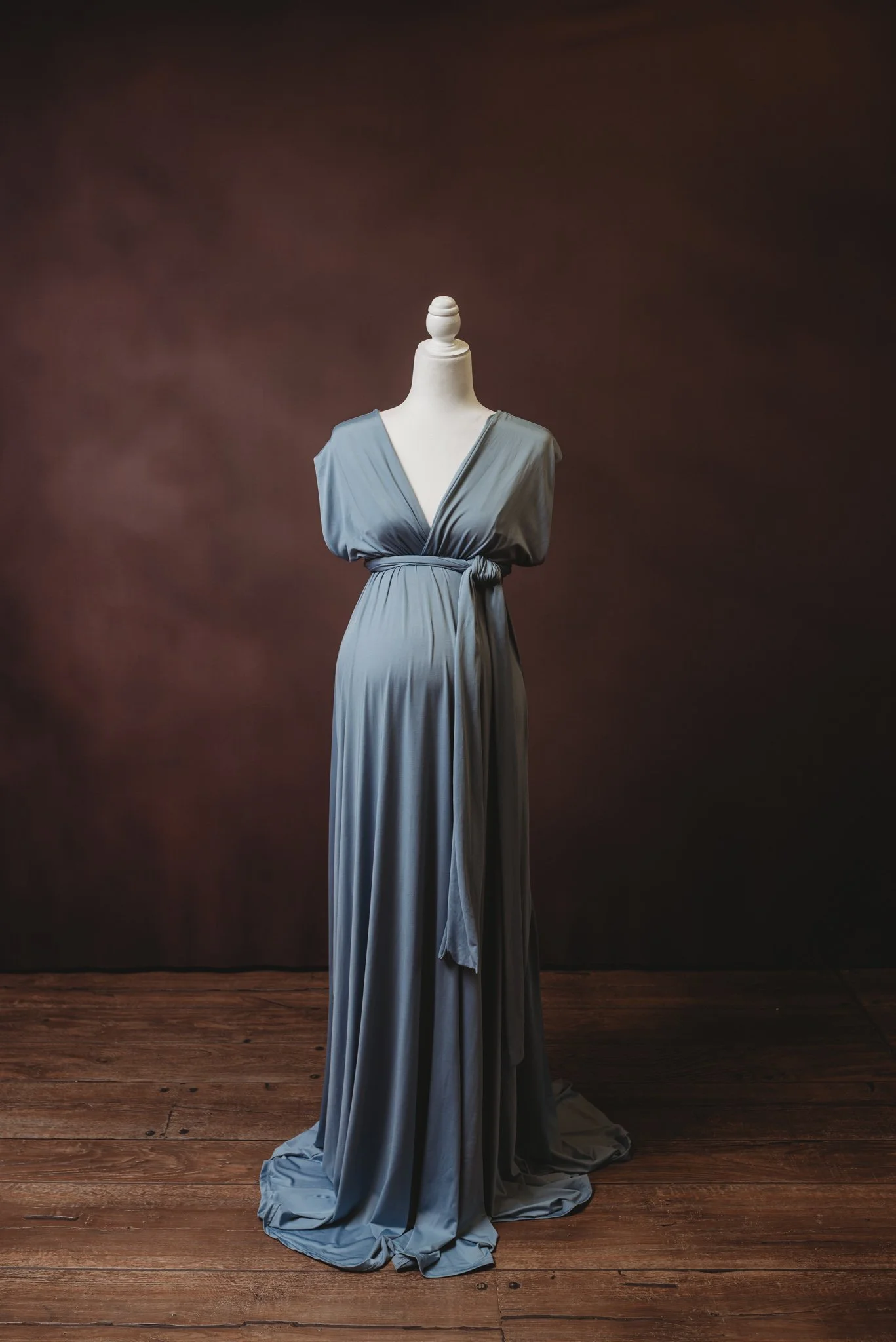 Mannequin displaying a blue floor-length gown with short sleeves and a V-neck, on a wooden floor with a dark background.
