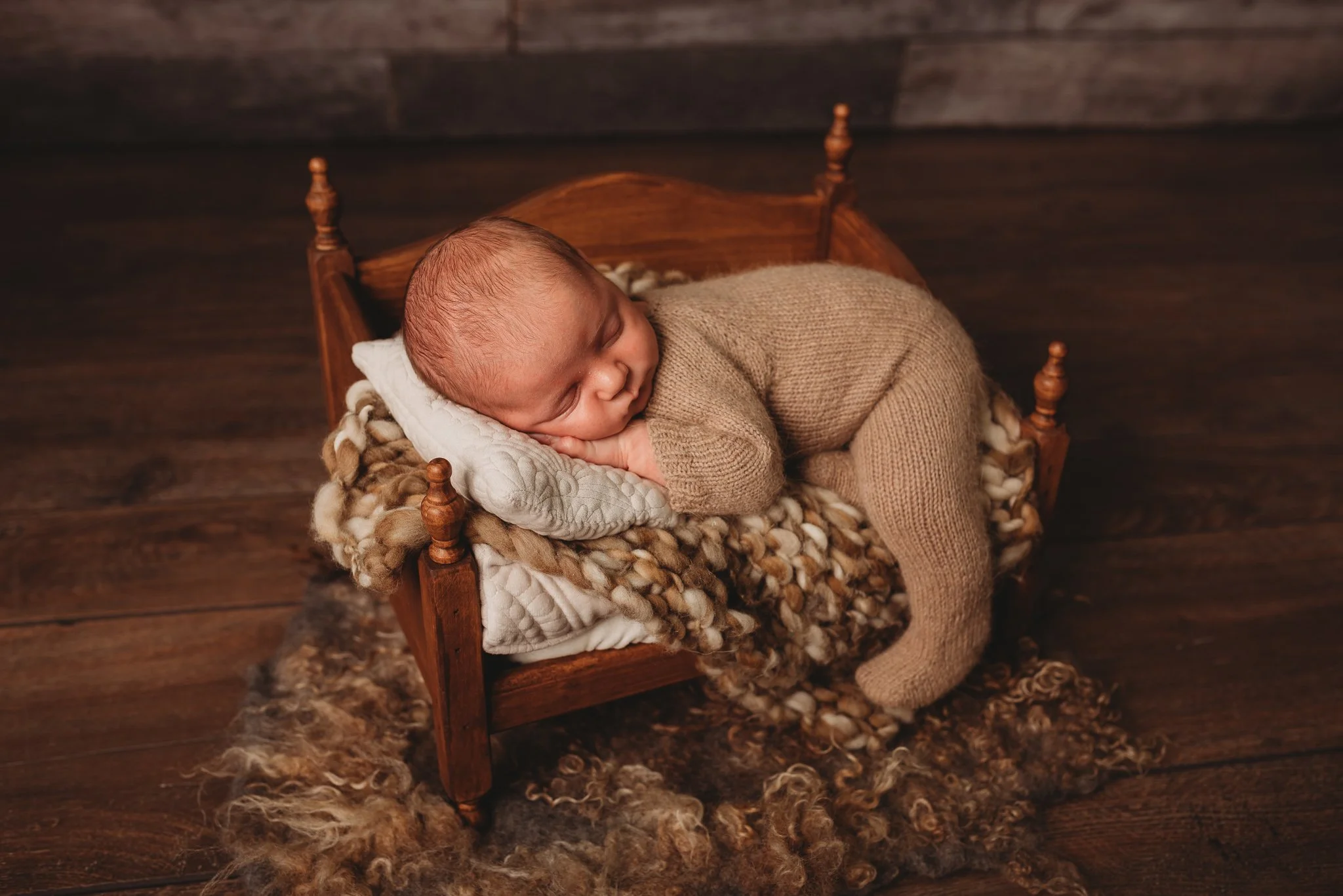 Newborn baby in knitted outfit sleeping on small wooden bed with blankets