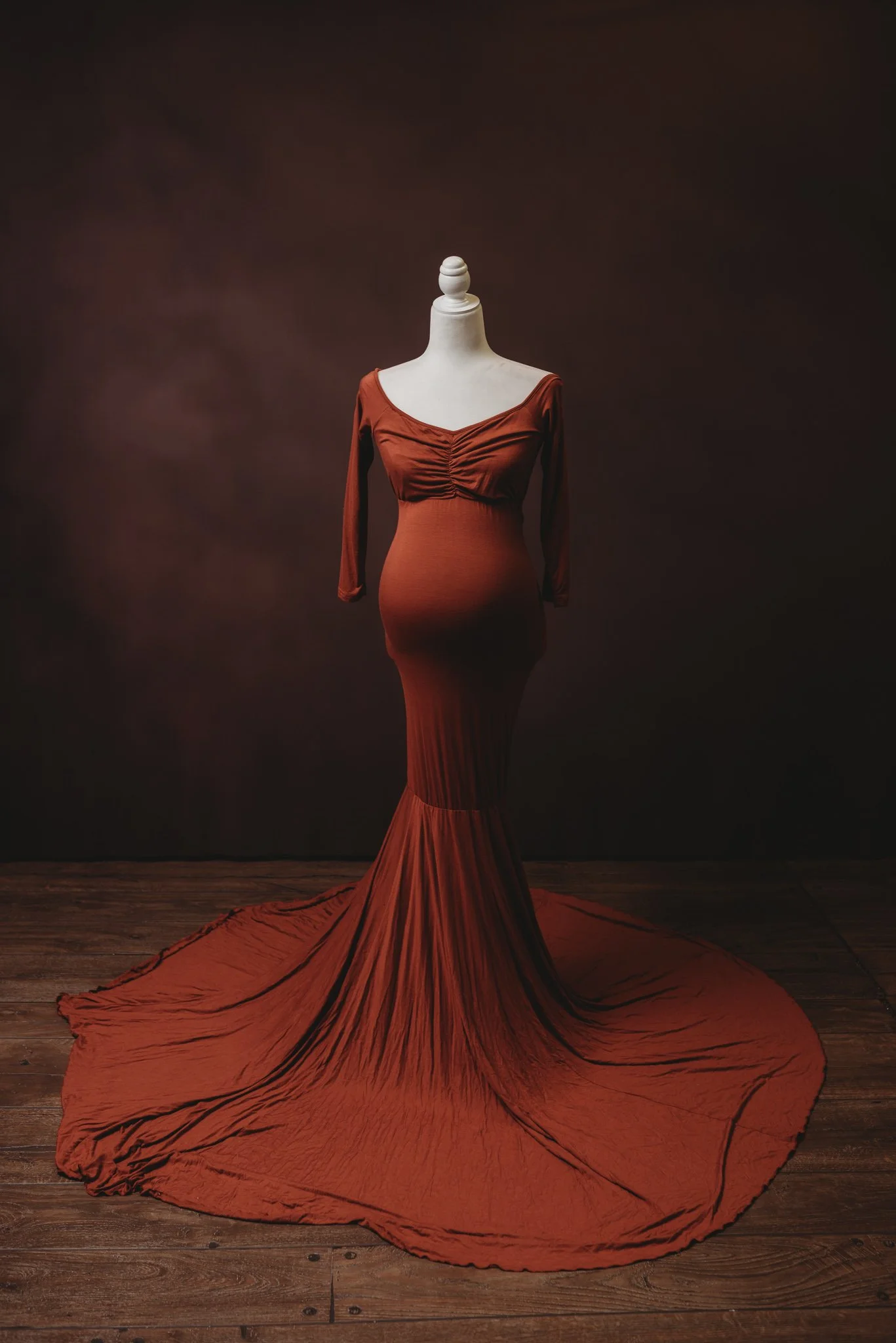 rust-colored, long-sleeved maternity gown on a mannequin against a dark background