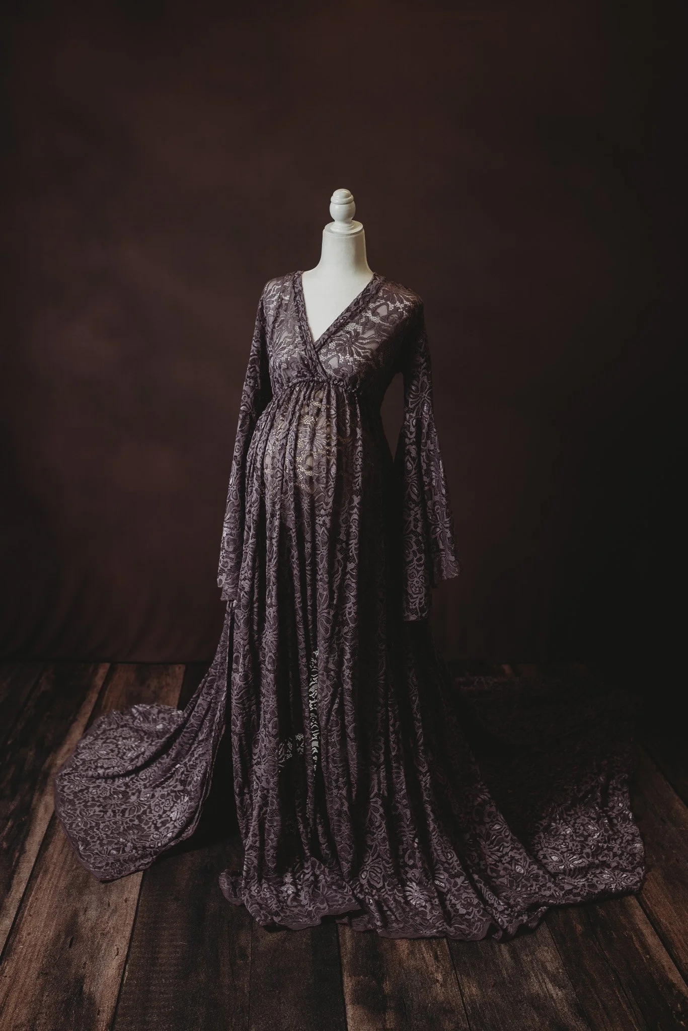 Mannequin wearing a long, dark lace maternity dress in a dark, moody setting.