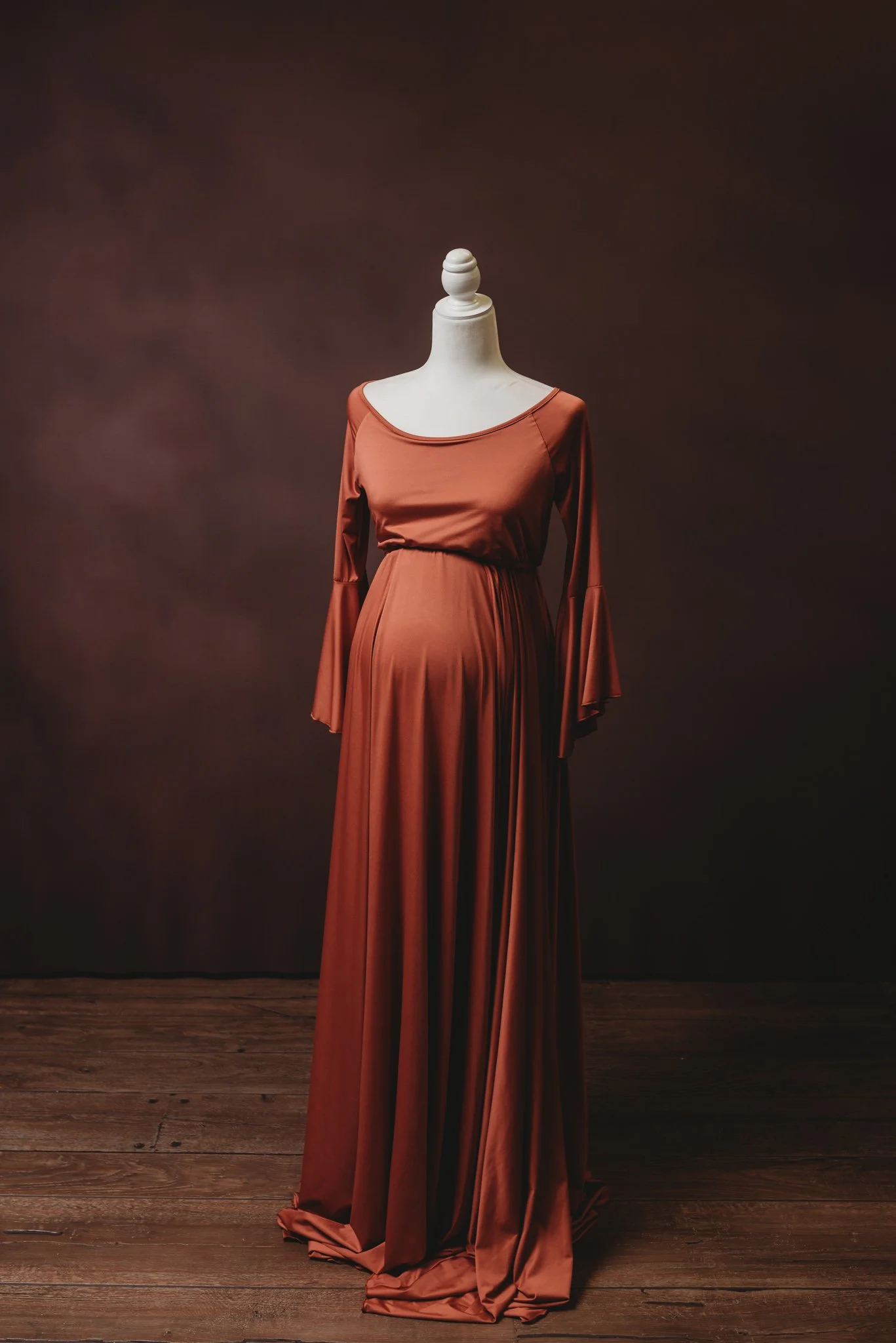 Mannequin displaying a maroon maternity dress with long sleeves on a wooden floor background.