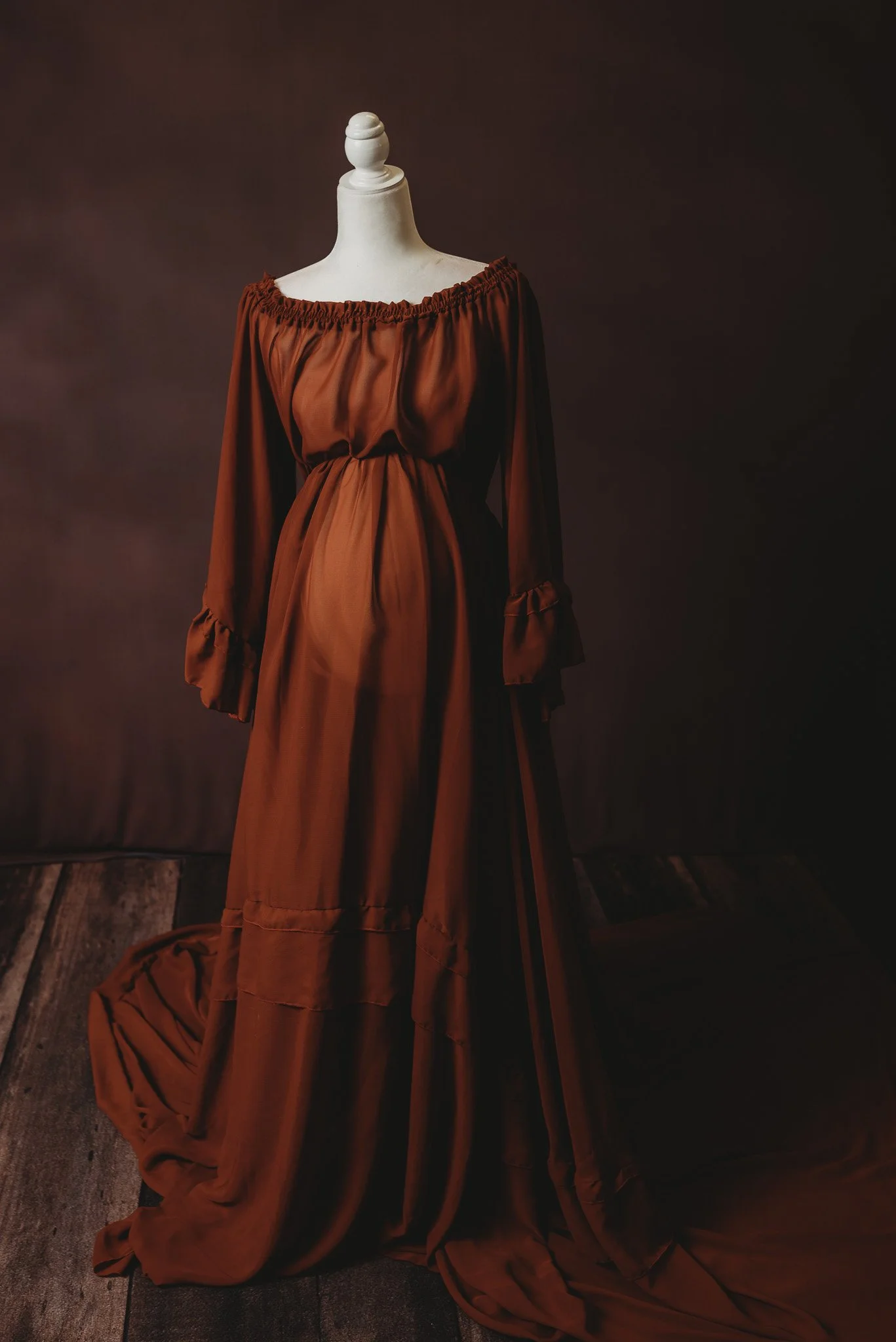 Mannequin wearing a flowing brown gown with off-shoulder design.