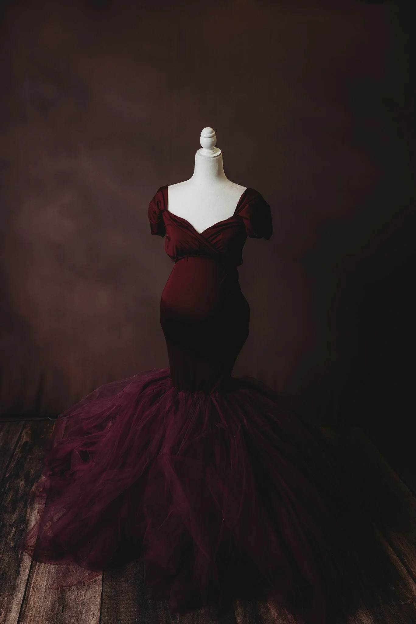 Dark red maternity gown on a mannequin against a dark background.