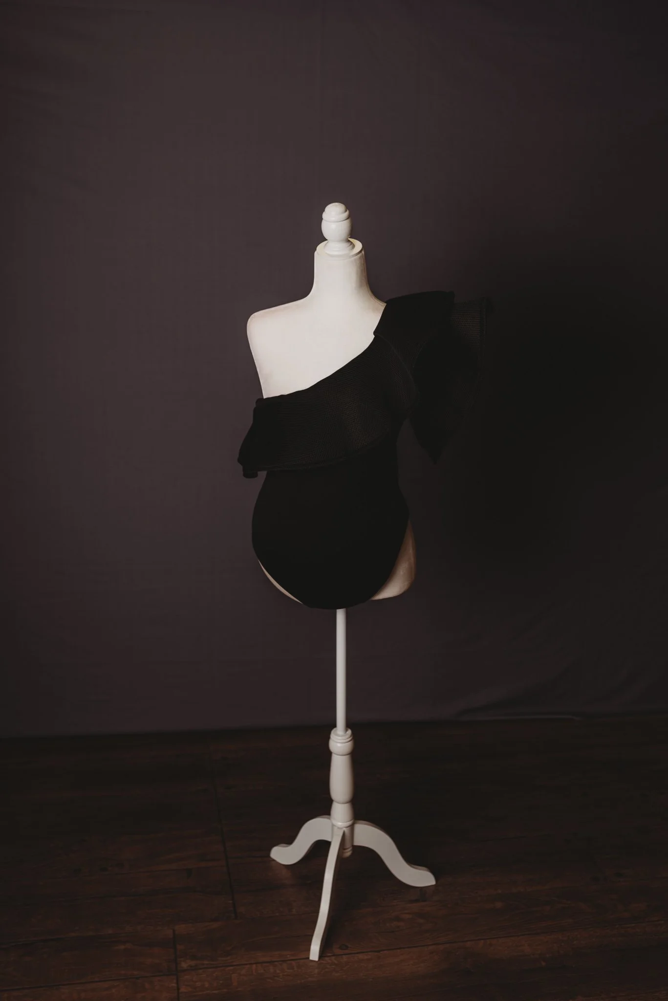 Mannequin displaying black one-shoulder dress in dark room