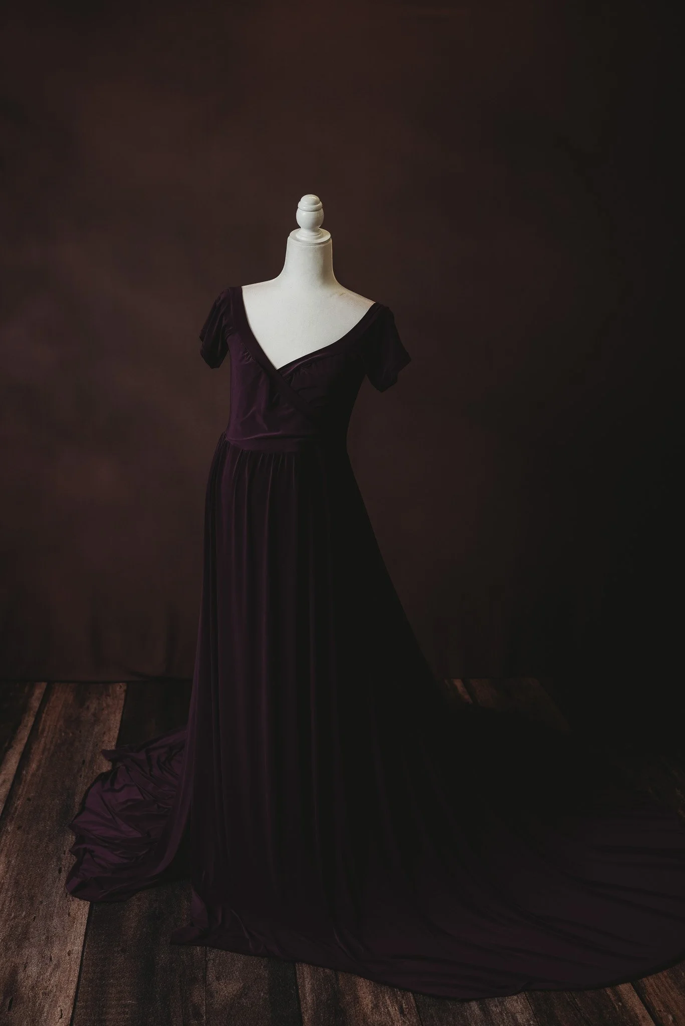 Elegant dark purple gown displayed on a mannequin against a dark background.