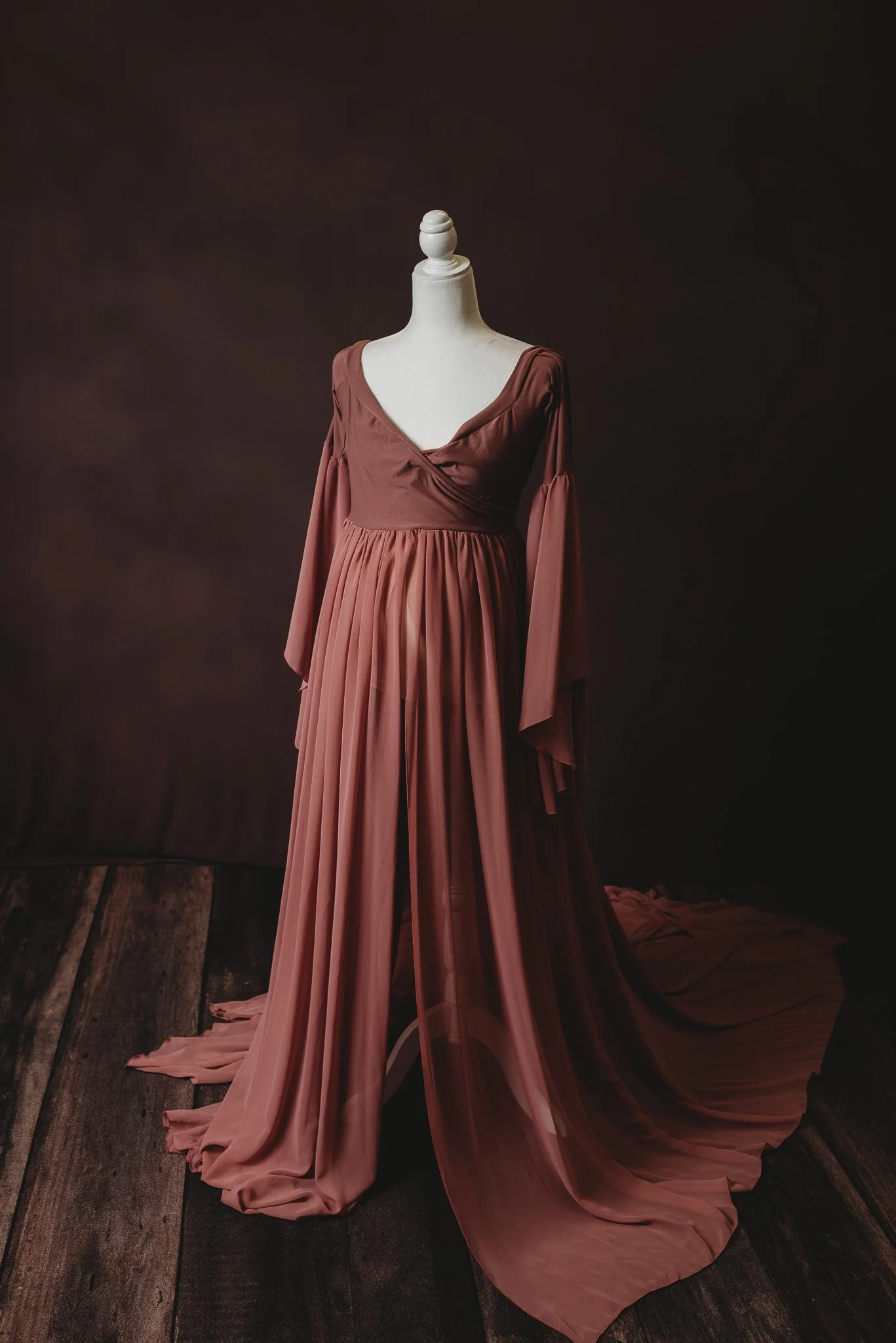 Mannequin displaying a flowing, long-sleeved, rust-colored maternity gown with a V-neckline.