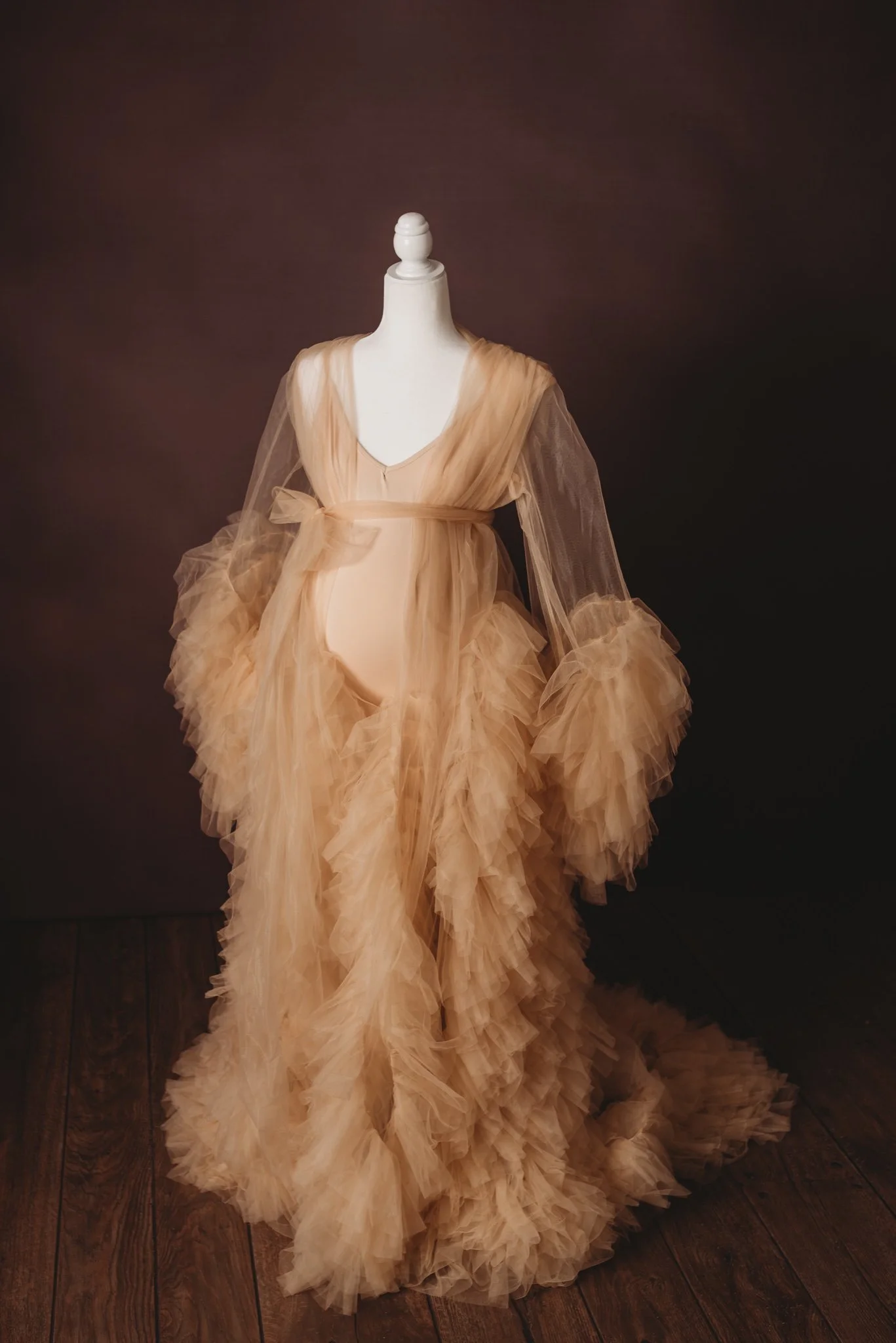 Elegant beige tulle gown on a dress form against a dark background.