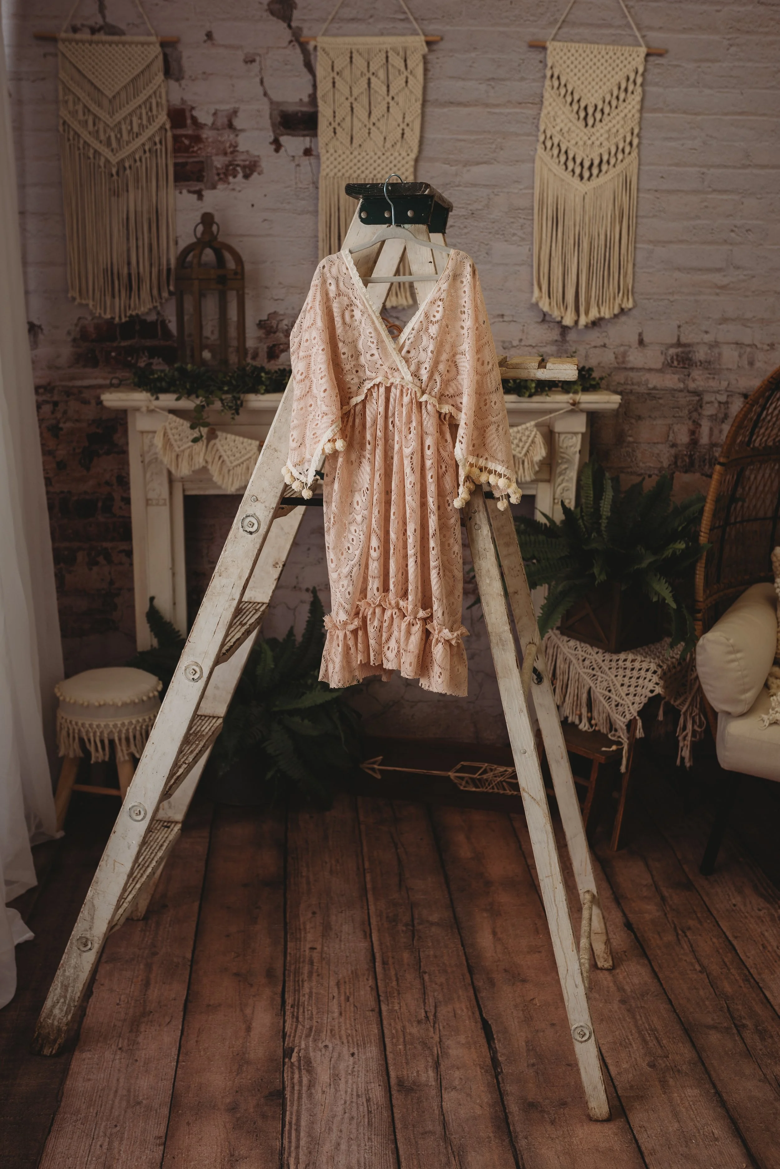 Bohemian styled peach dress hanging on a wooden ladder with macramé wall hangings and rustic decor.