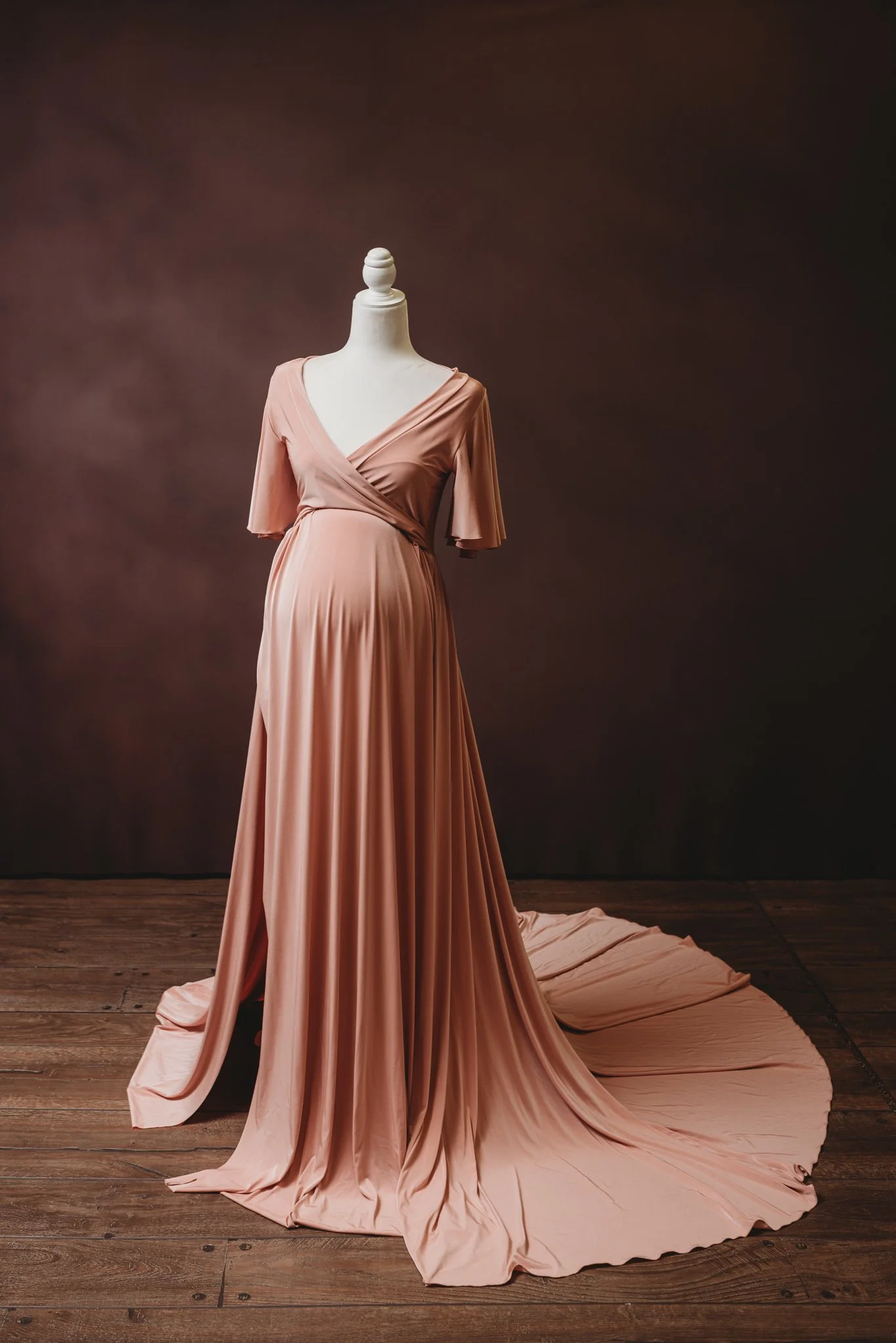 Elegant maternity dress displayed on a mannequin with a long flowing skirt in a studio setting.