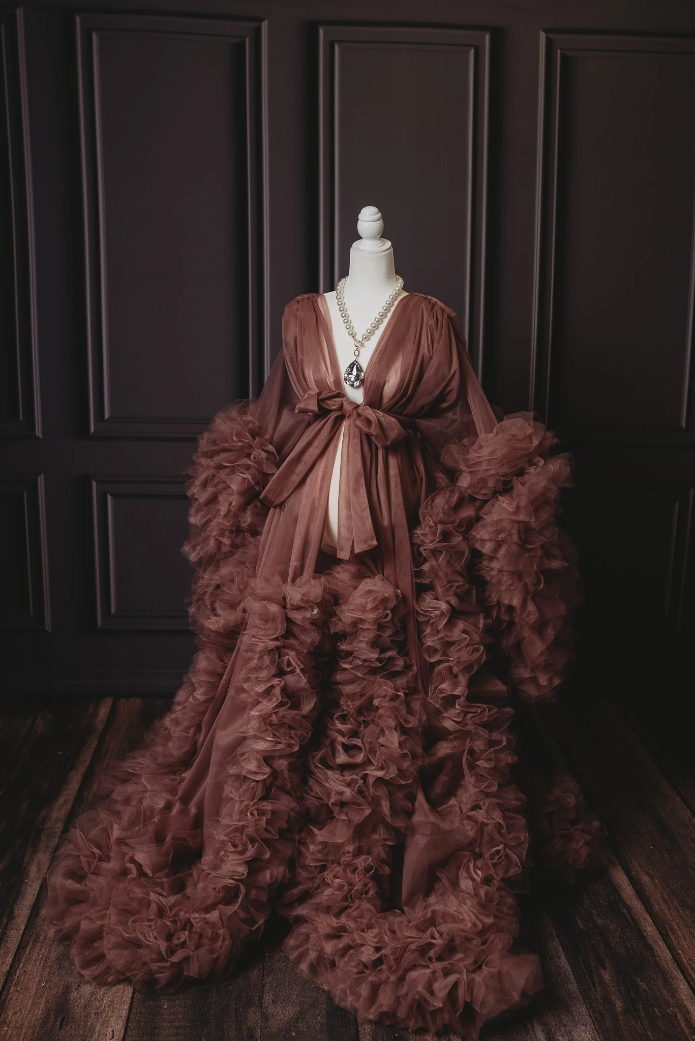 Elegant brown tulle gown with ruffled layers on a mannequin, set in a dark wood paneled room.