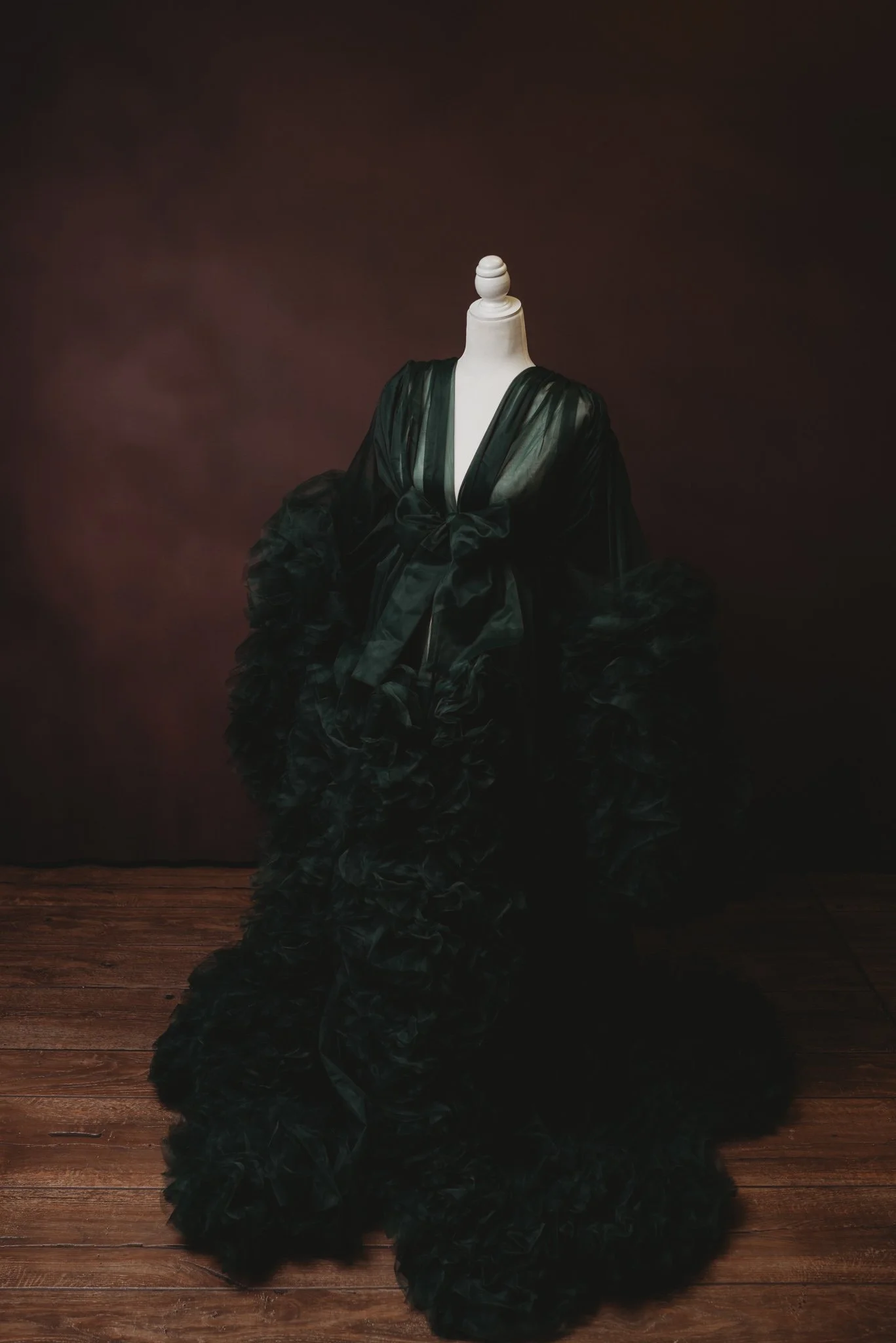 Dark green ruffled gown on a mannequin against a dark background.