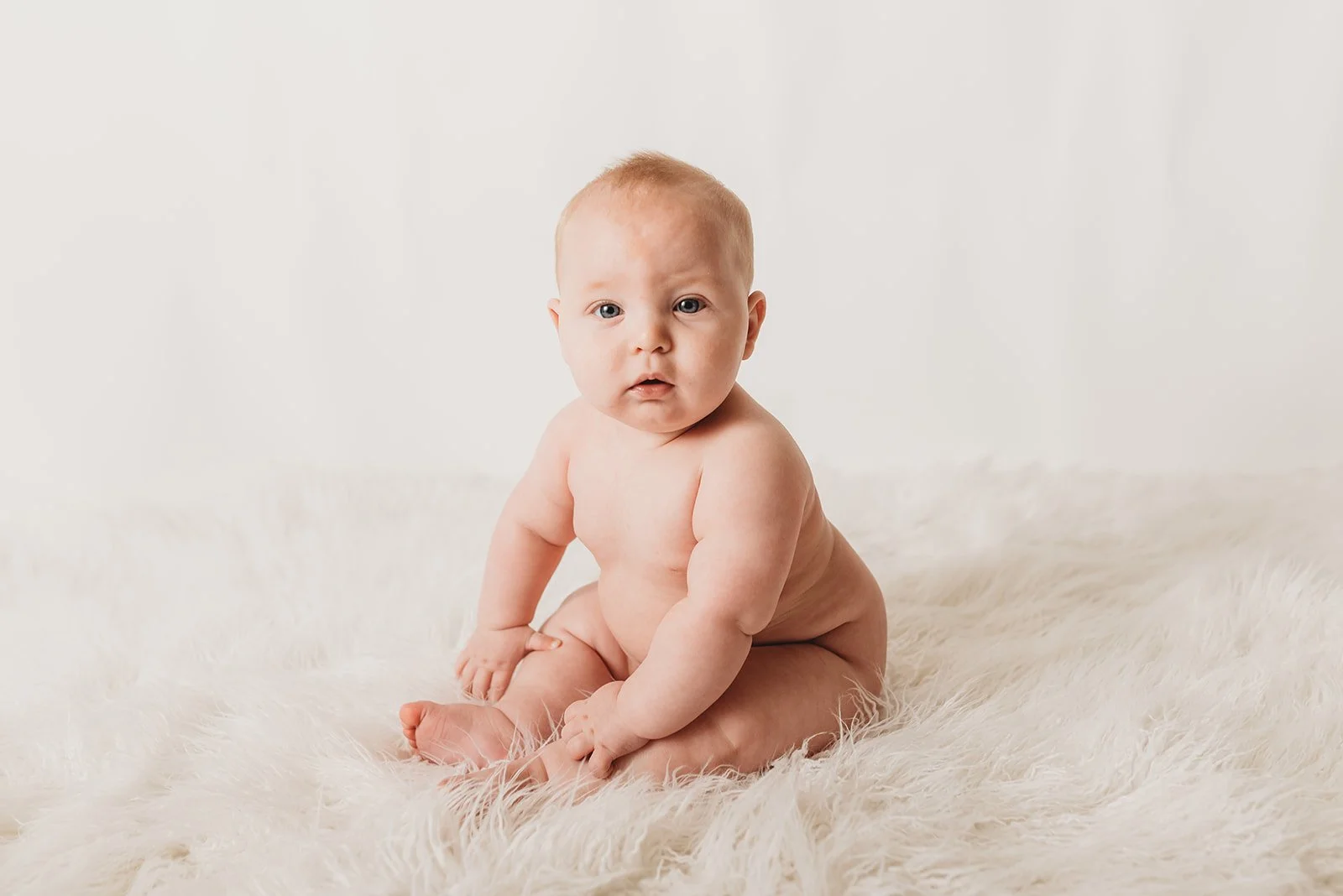Naked baby sitting on white fluffy rug
