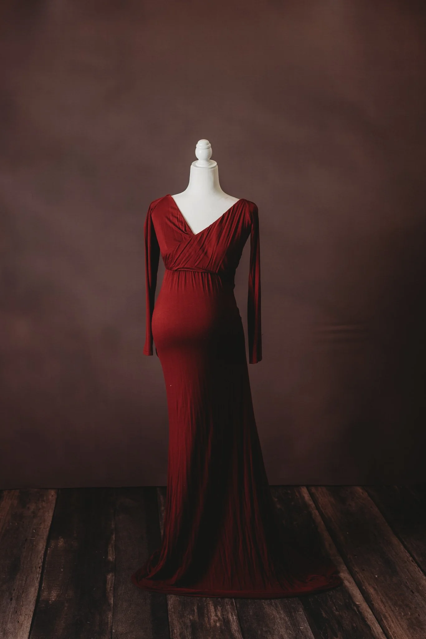 Elegant burgundy maternity dress on a mannequin against a dark background.