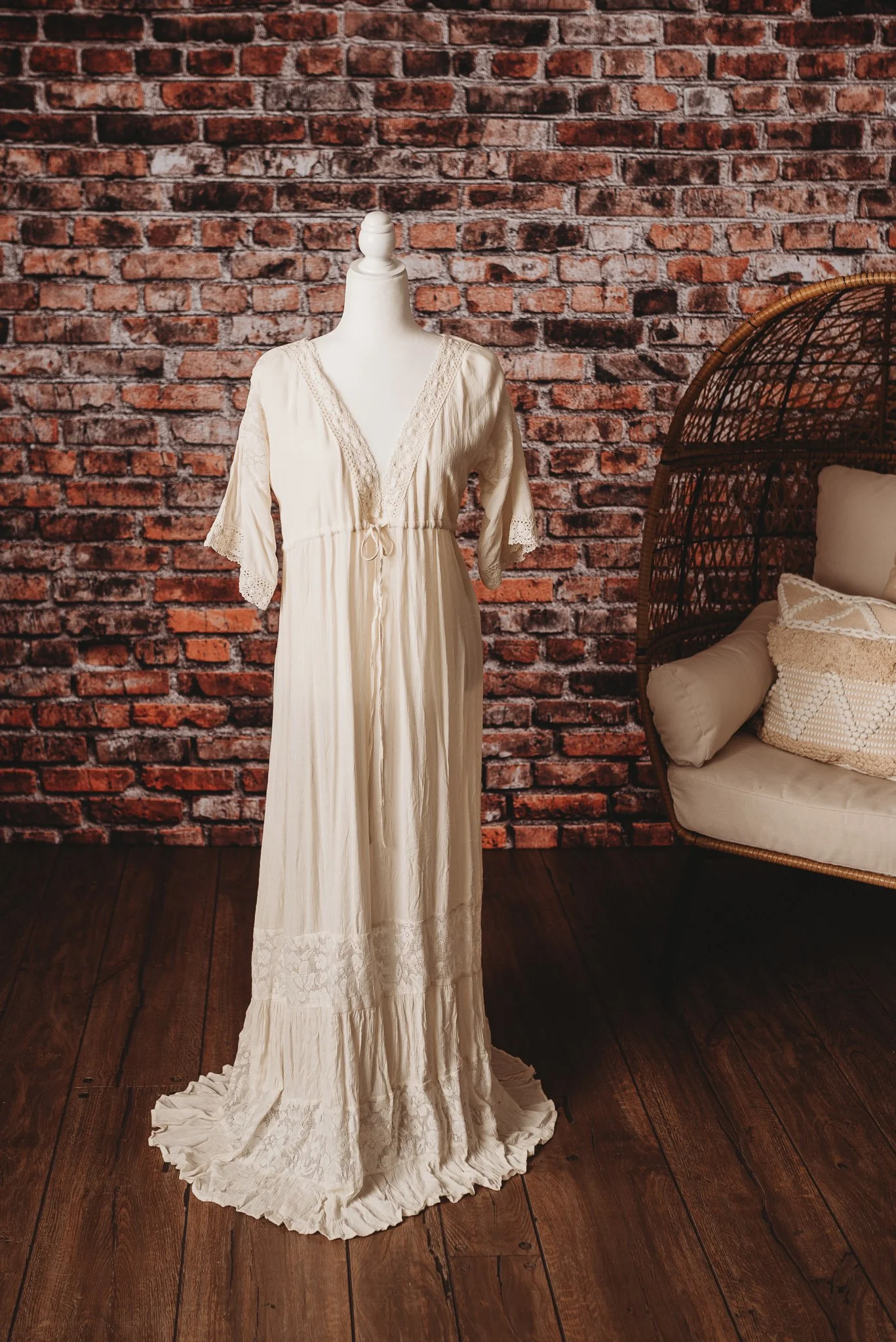 Ivory lace dress on mannequin with brick wall background and wicker chair
