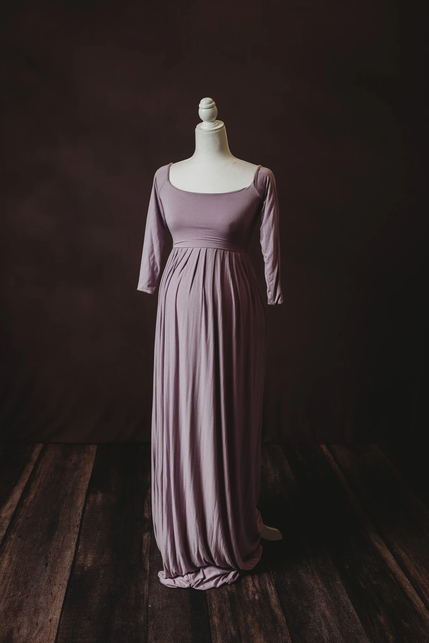 Purple maternity dress on mannequin with dark background.