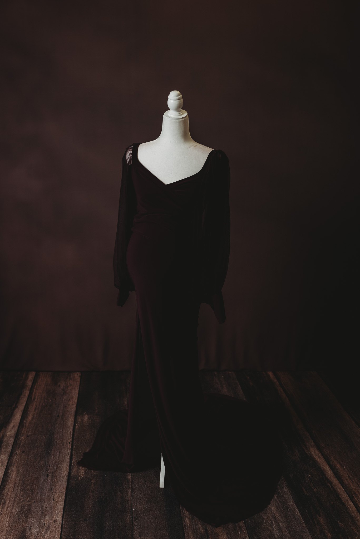 Dark long-sleeved dress on white mannequin against dark background.