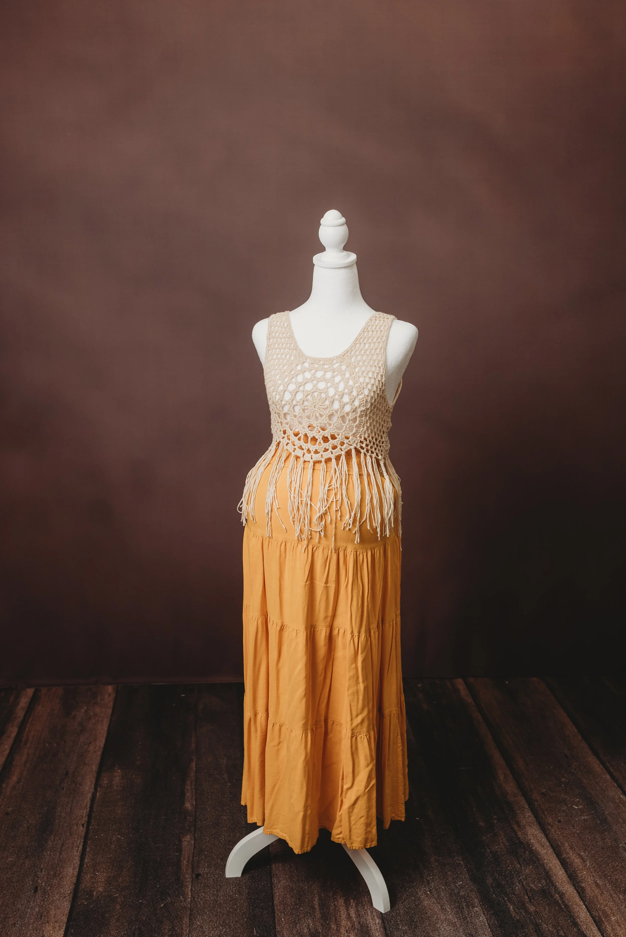 Mannequin dressed in a crochet top and a yellow maxi skirt, displayed on a white stand against a brown background with wooden floor.