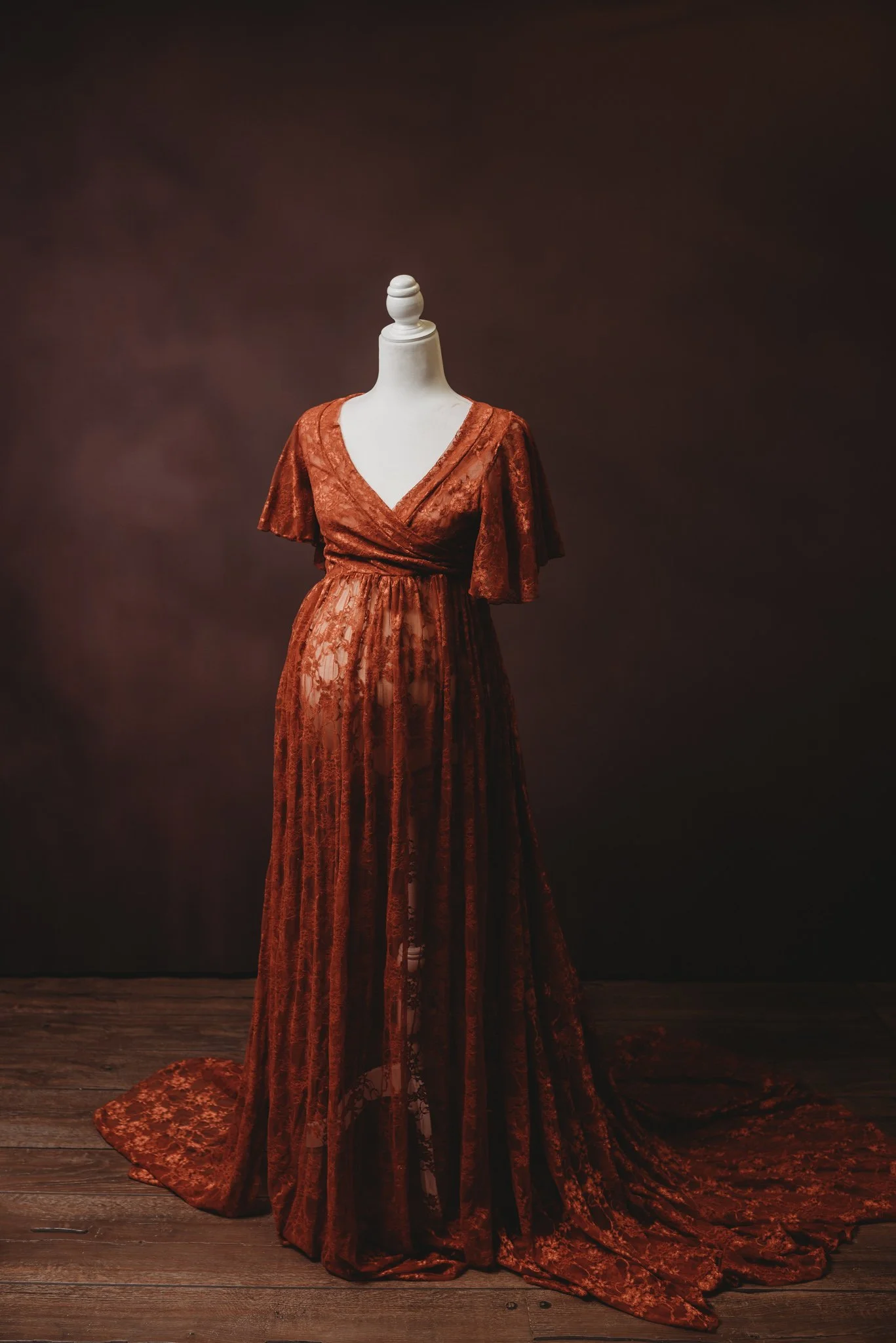 Mannequin wearing a long, flowing, reddish-brown lace dress with a V-neck and short sleeves.