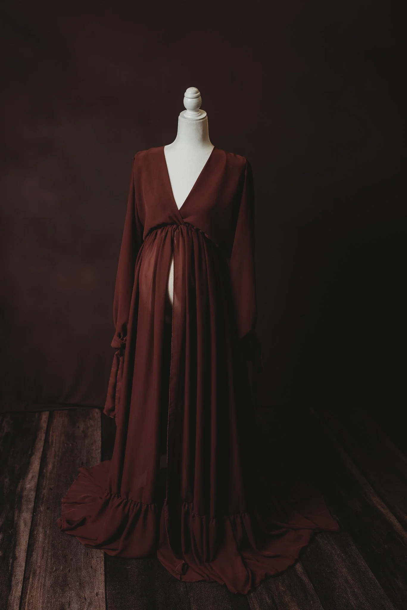 Mannequin wearing a long, dark burgundy dress with ruffled hem on wooden floor.